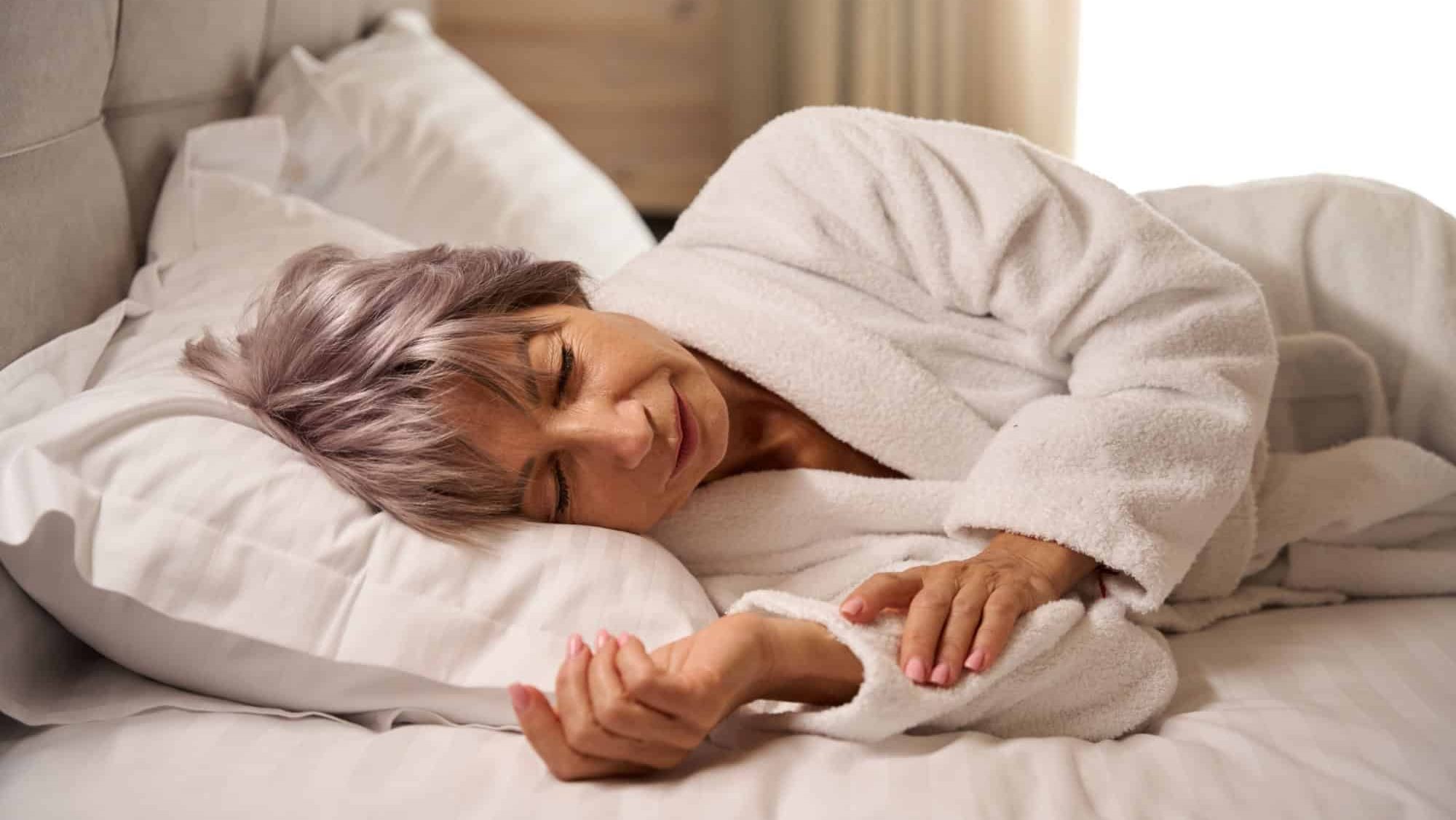 Elderly woman sleeps sweetly in bright bedroom on soft pillows