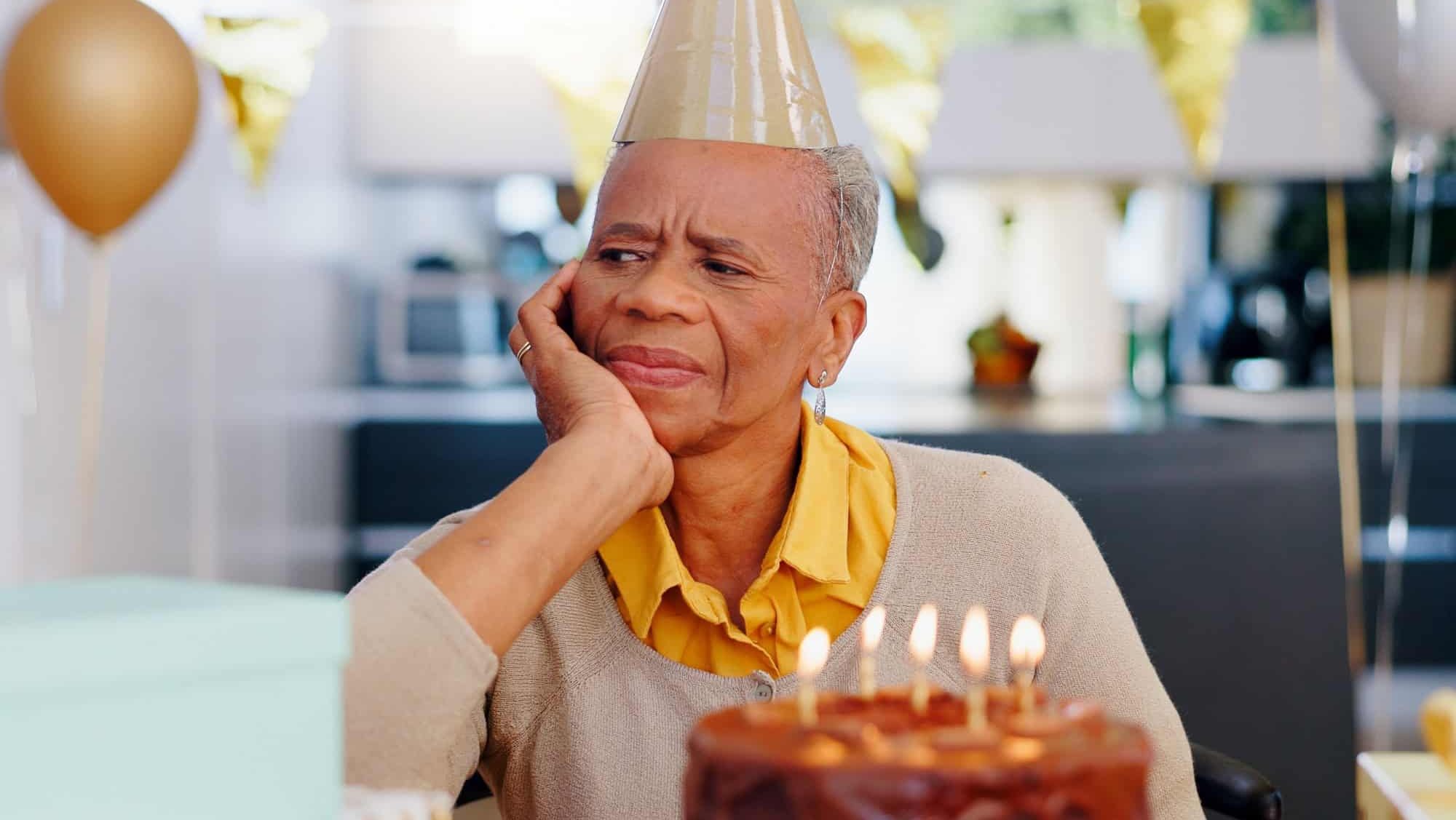 Sad, birthday and senior woman thinking with depression, grief and lonely in her home. Cake, face and elderly African person alone at a party with disappointment, frustrated or annoyed in a house