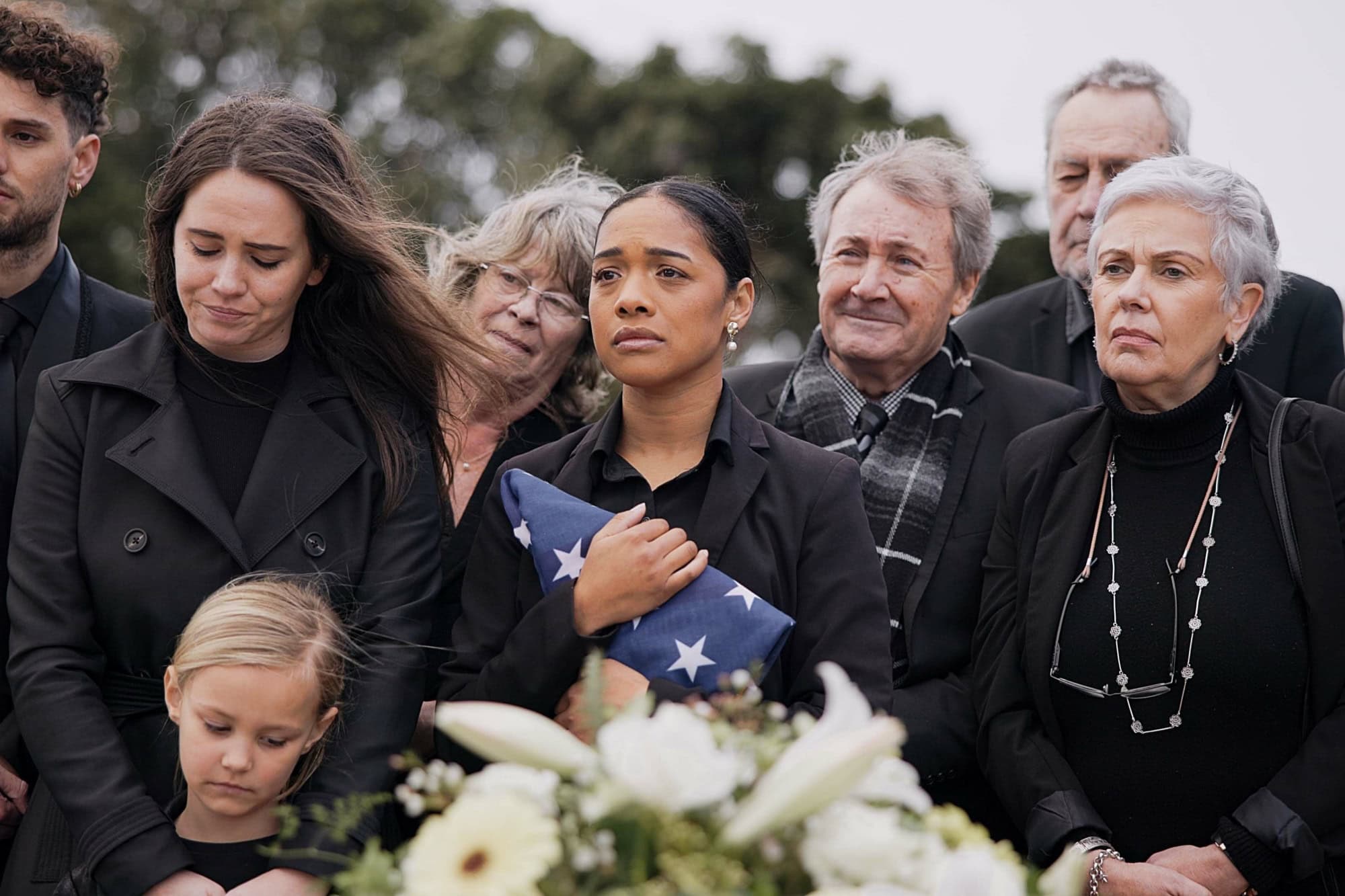 Funeral, cemetery and family with American flag for veteran for respect, ceremony and memorial service. Sad, depression and people by coffin in graveyard for military hero, army and soldier mourning