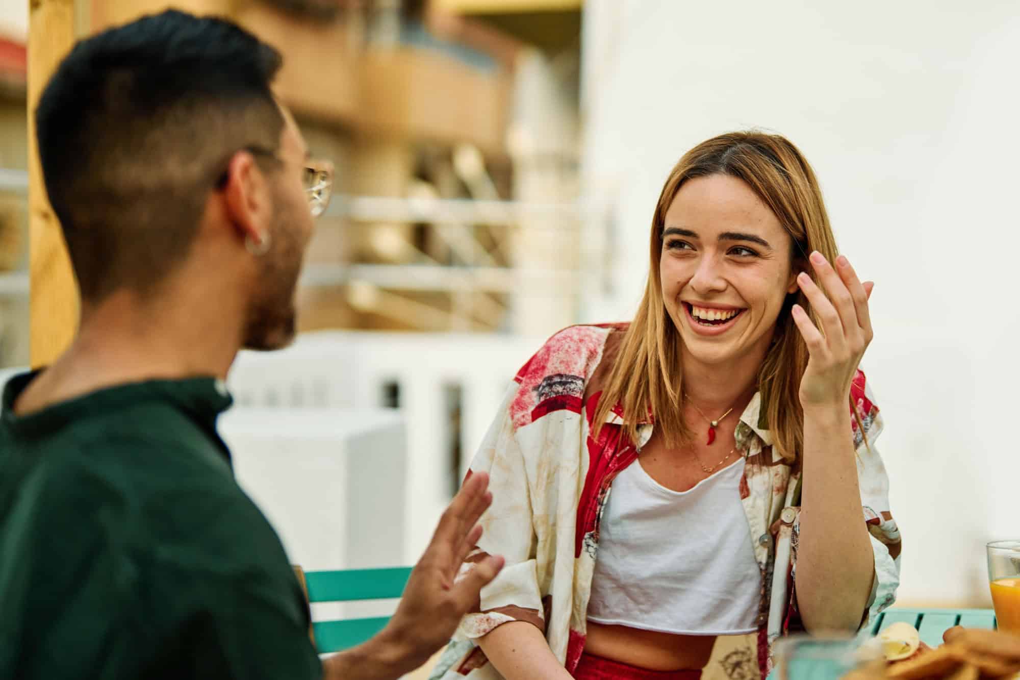 Happy young couple having fun during a rooftop party during a summer holiday, sitting by the table talking, eating and drinking, love, romance, relationship, flirting and youth culture concept