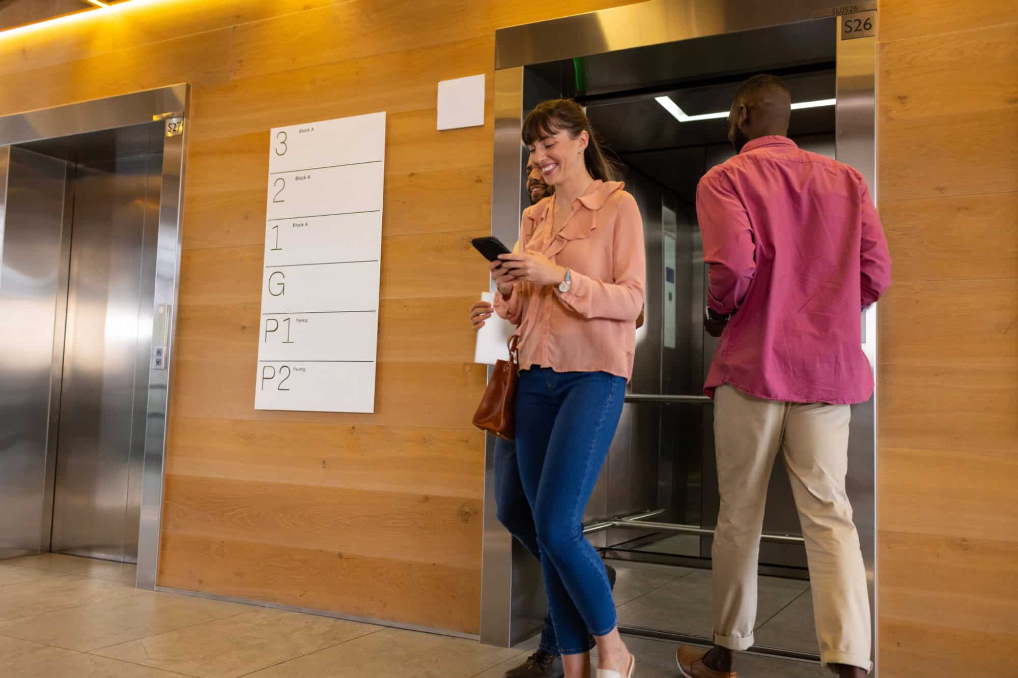Using smartphone, woman walking past man entering elevator in office building. Technology, business, corporate, hallway, communication, professional