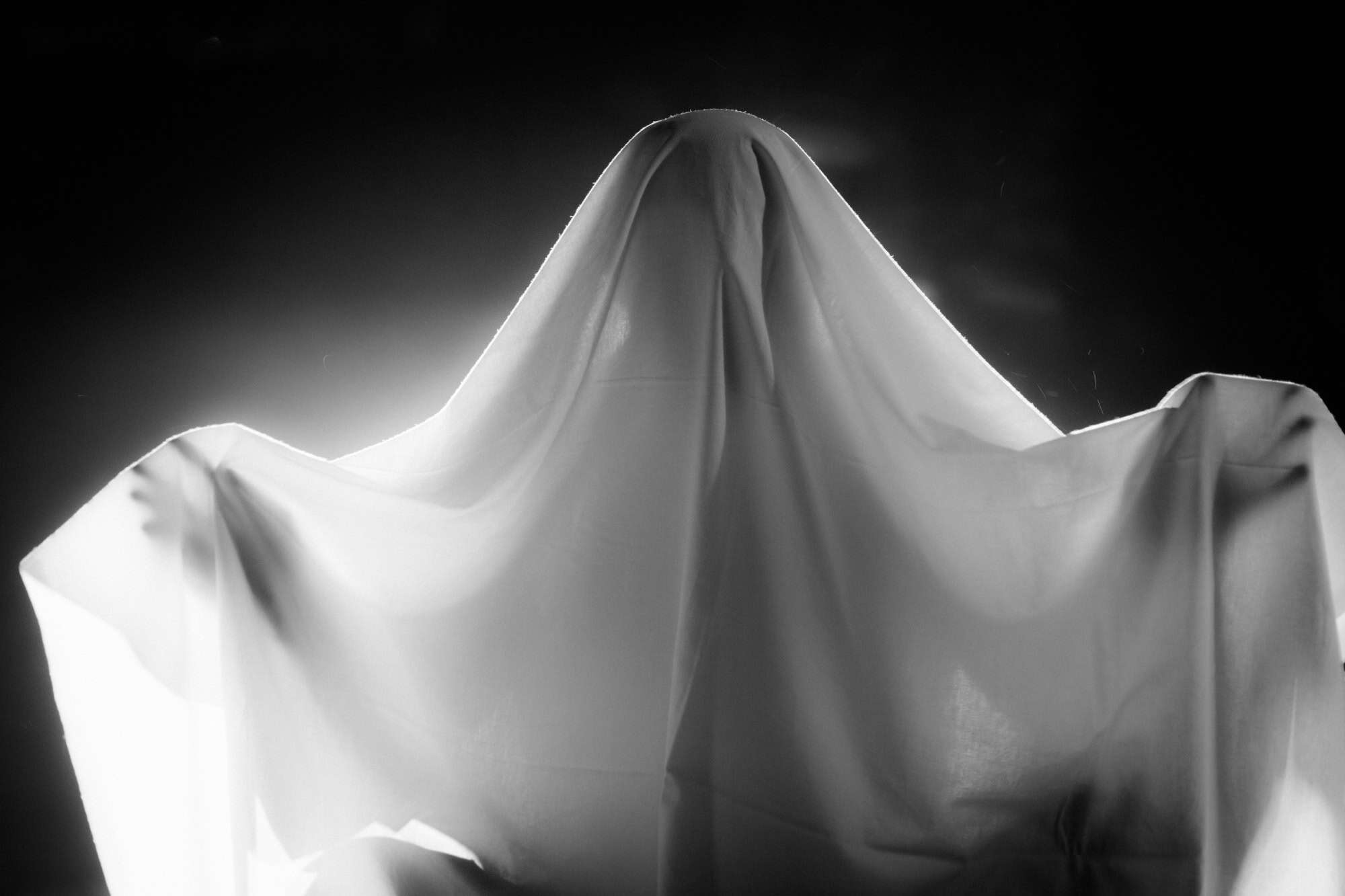 Silhouette of a person covered with a white sheet against a dark background, creating a mysterious and artistic image.