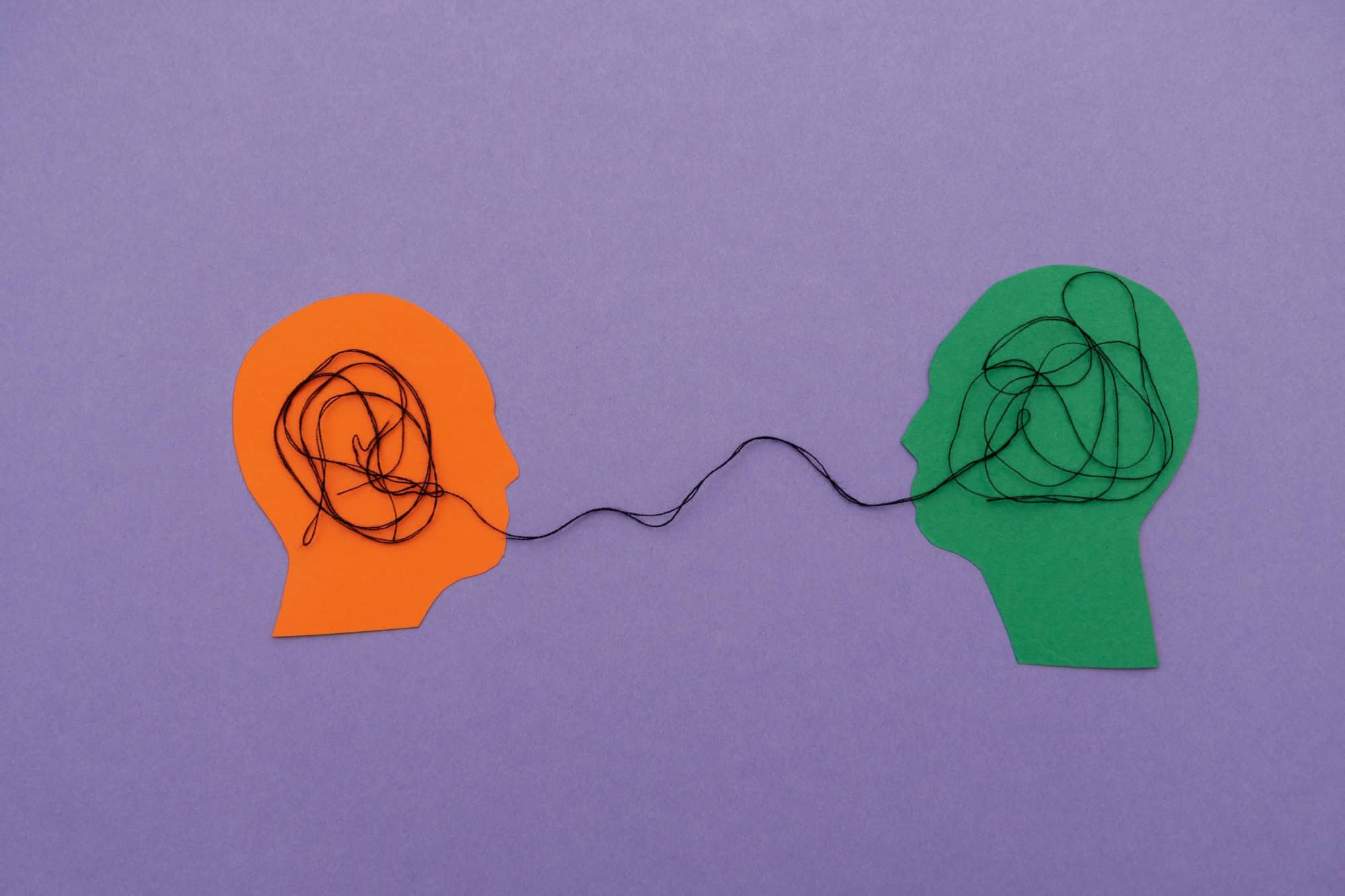Two colorful human head silhouettes Connected by tangled Thread on purple background, Symbolizing Communication and Understanding