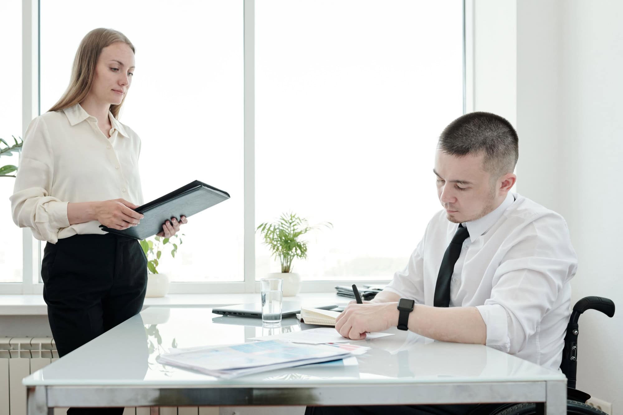 Young secretary looking at boss signing document by table