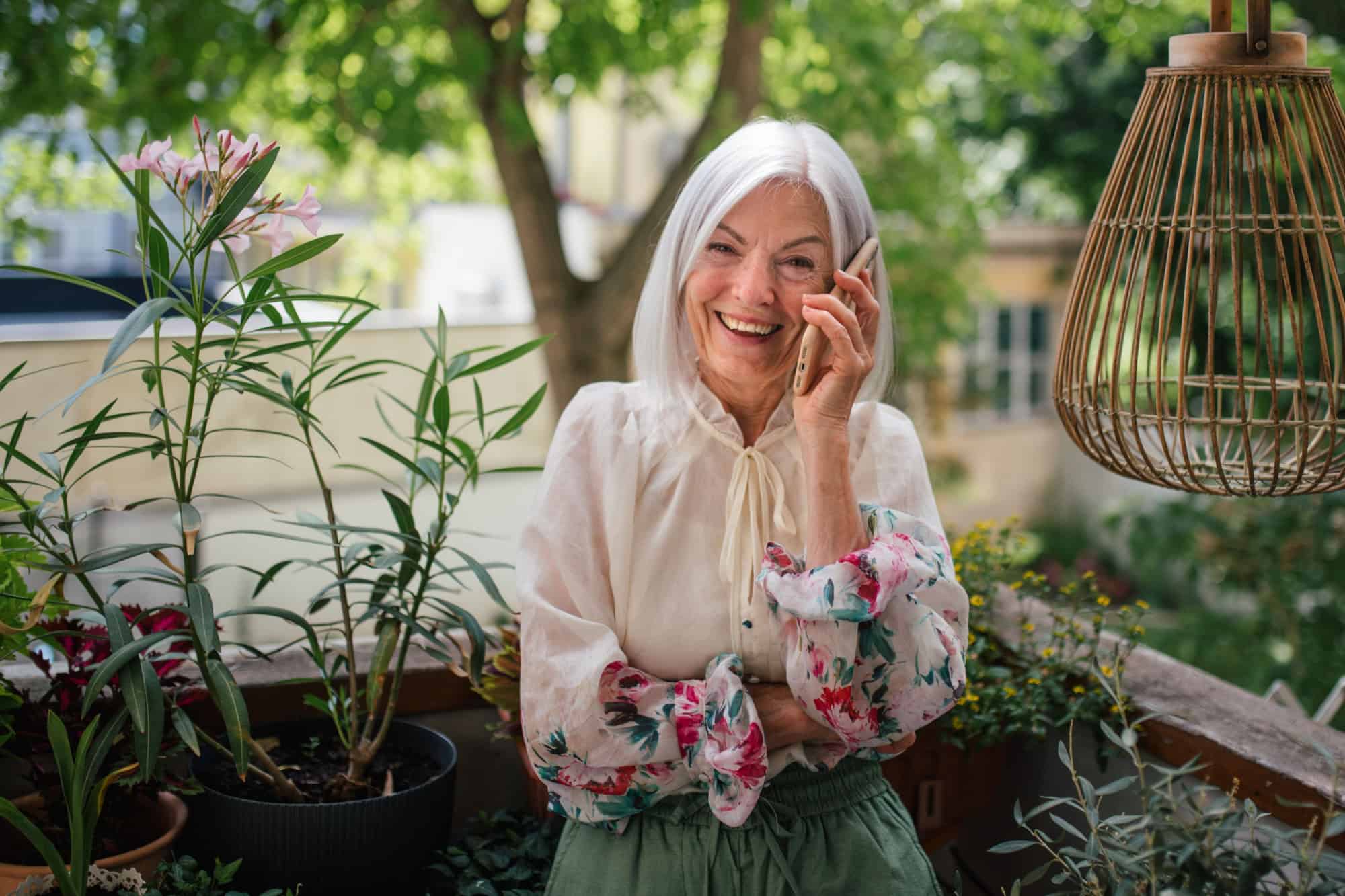 Portrait of beautiful senior woman standing on balcony and making phone call.