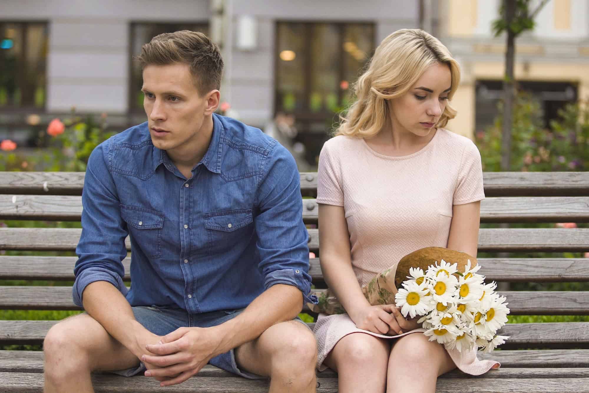 Unhappy couple sitting after fight, girl with flowers, problem in relationship