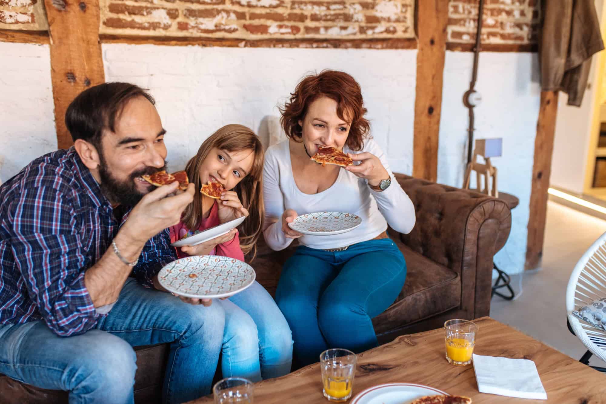Happy family at home in the couch eating pizza