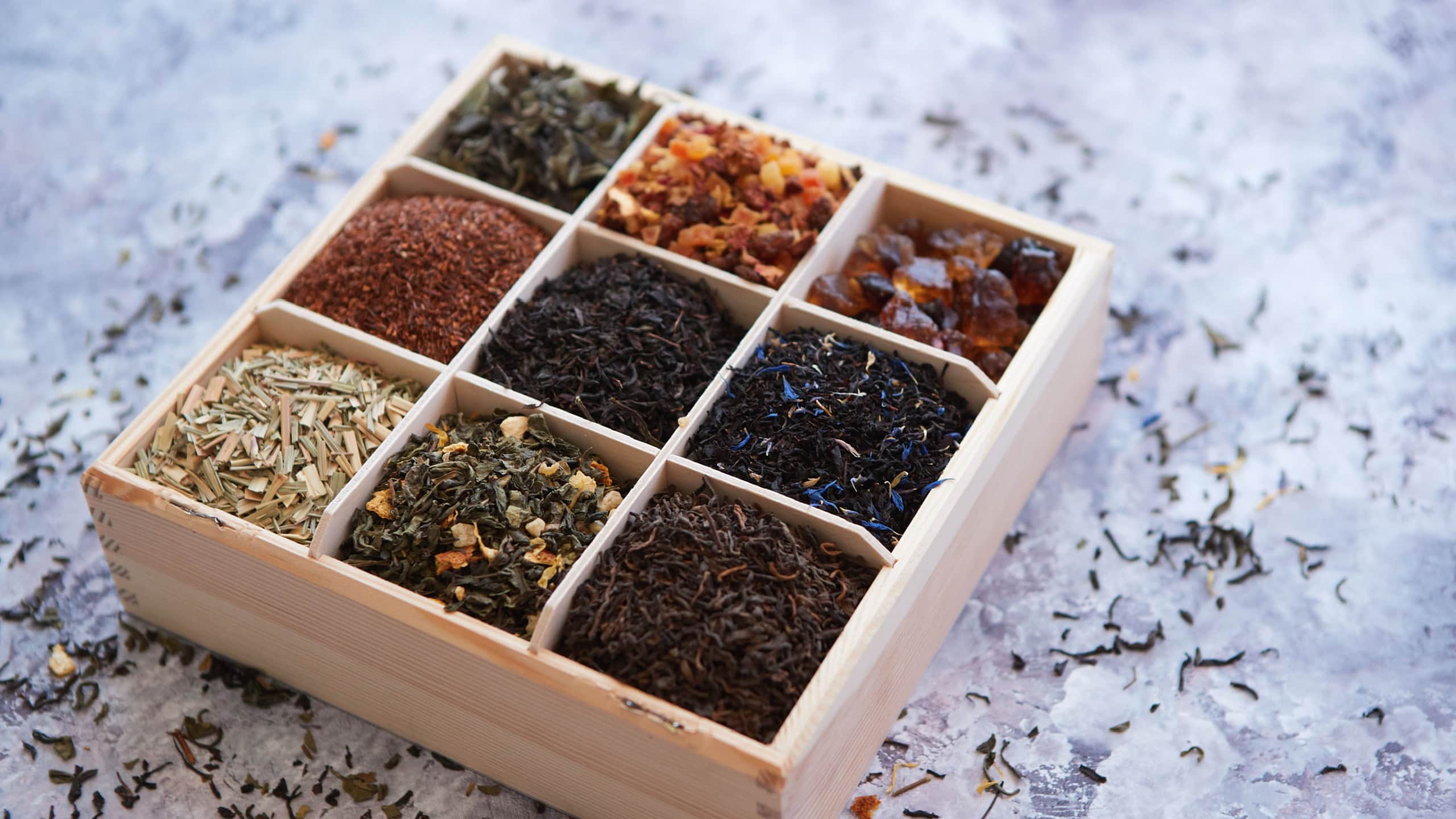 Various kind of dry tea - green, black, red, fruit and blue in wooden box on the table. Top view. Tea time concept.