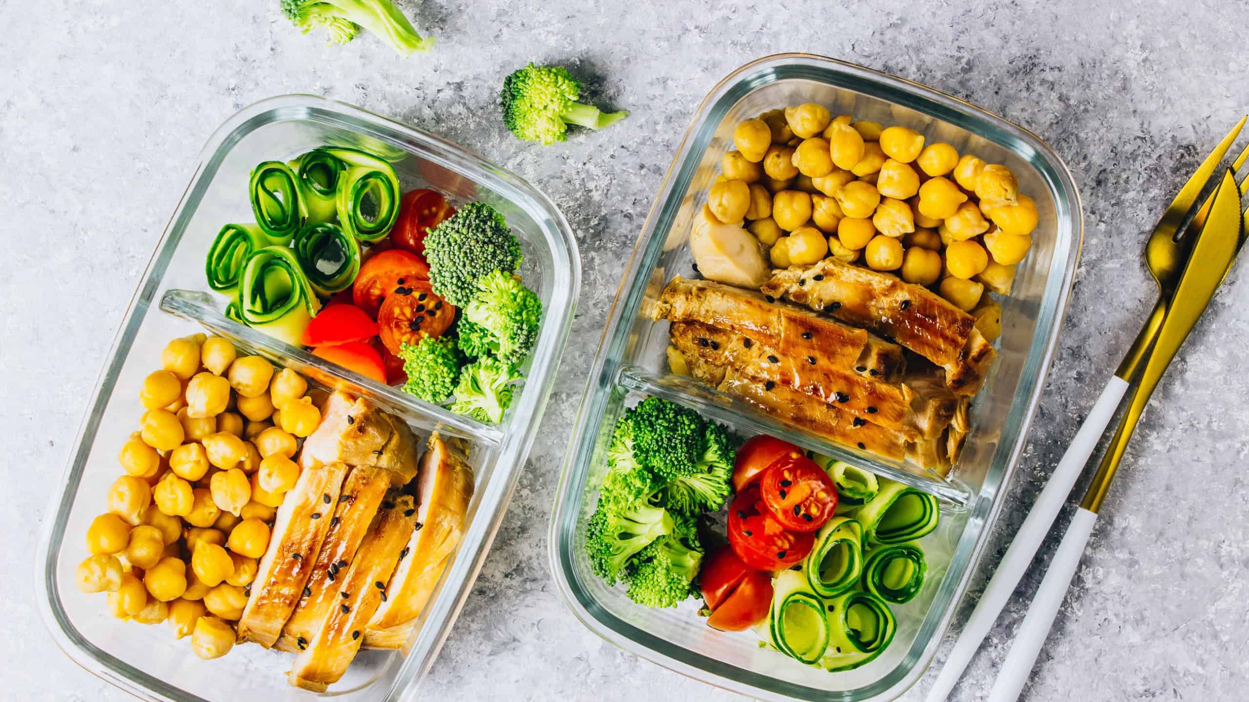 Healthy meal prep containers with chickpeas, chicken, tomatoes, cucumbers, avocados and broccoli. Top view