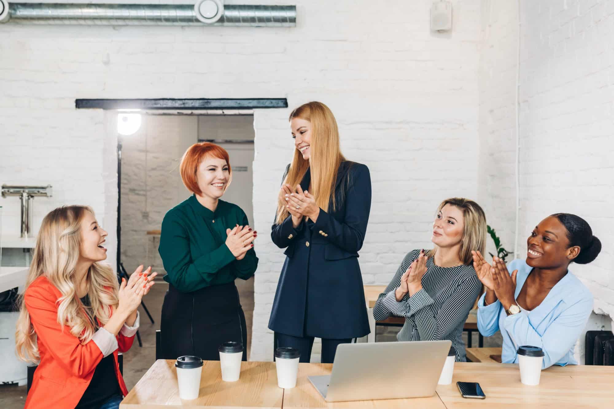 Shy female applicant arriving at job clapping hands with the others while receiving greeting of her new colleagues making good first impression at meeting with new partners, women in business