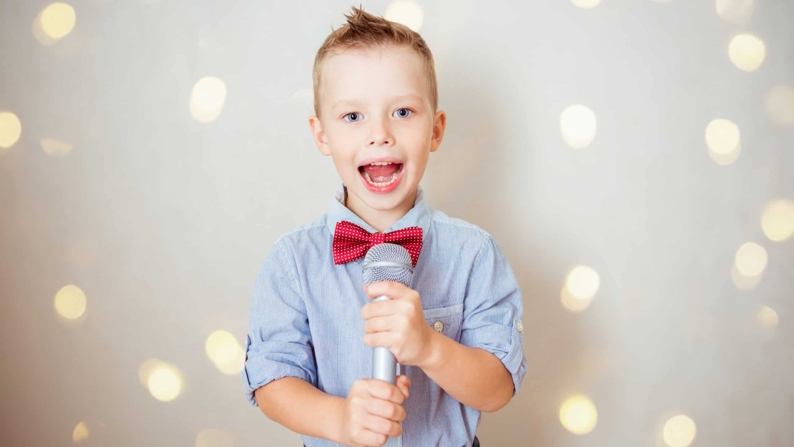 Little boy singing with microphone on gray background. Music, song and education concept