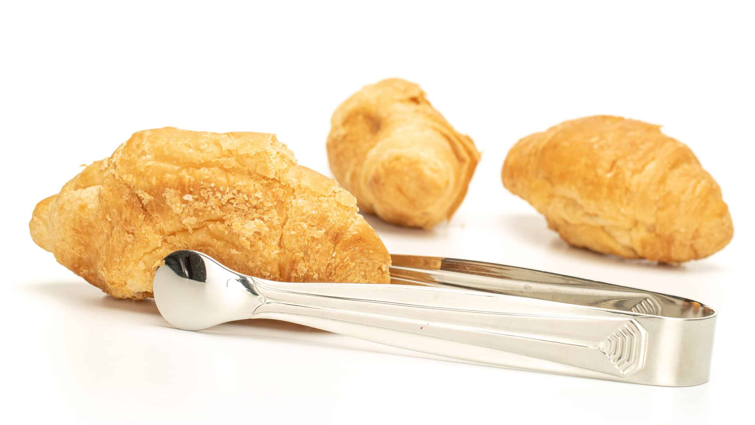 Group of three whole fresh baked mini croissant with sugar tongs isolated on white background