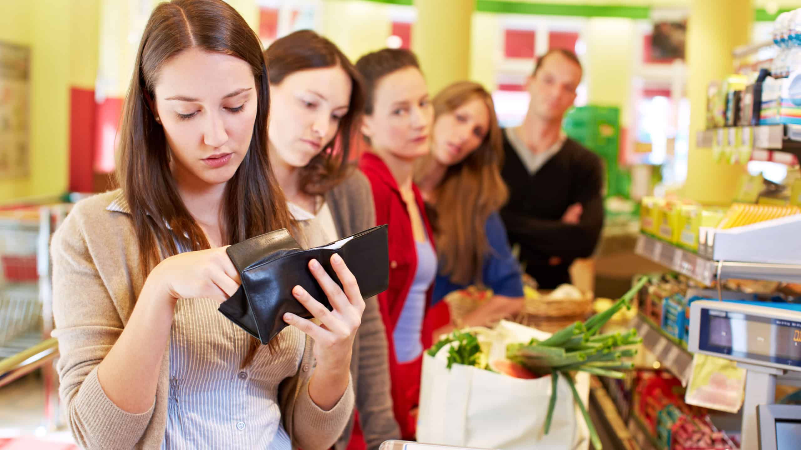 Woman is looking for her money at the supermarket checkout with long queue behind her