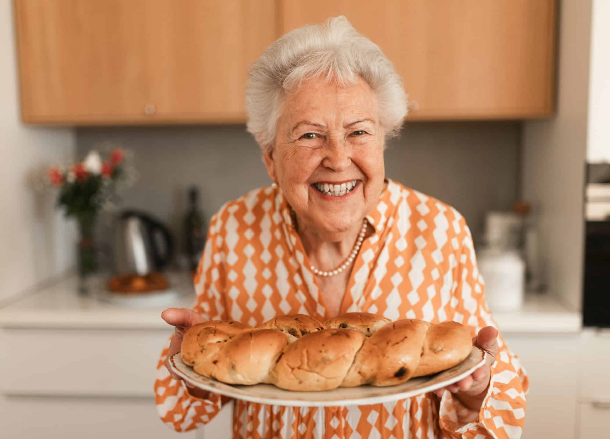 Happy senior woman with homemade sweet braided bread with raisins.