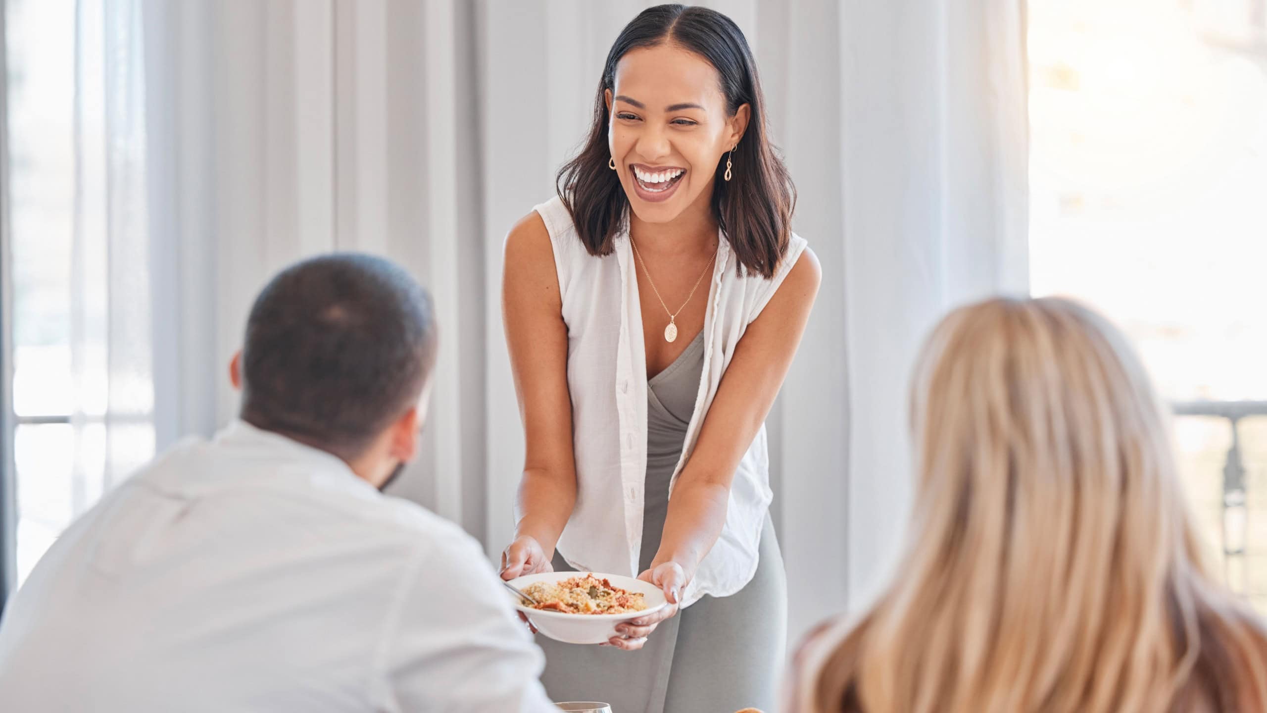 Home, food and happy hosting woman serving guests lunch in Mexico home with cheerful smile. Happiness, wellness and girl hostess holding health couscous salad at friends house gathering.
