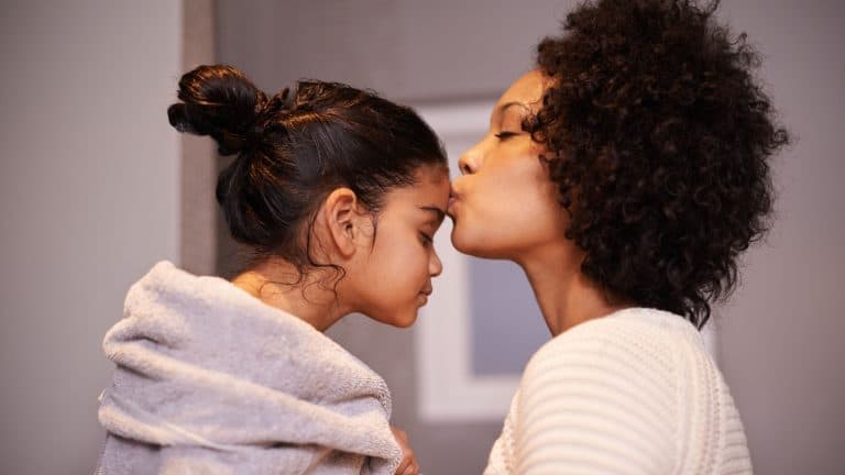 Love, kiss and mother with girl in a bathroom for cleaning, bonding and bonding after shower routine. Washing, towel and mom kissing forehead of child after bath, sweet and caring in their home