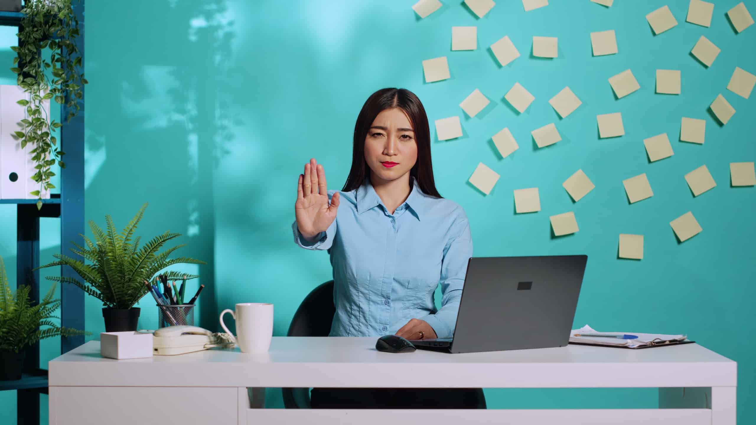Adamant uncompromising businesswoman saying stop throwing halt sign gesture, unhappy with work conditions. Assertive asian employee at colourful office desk over blue studio background