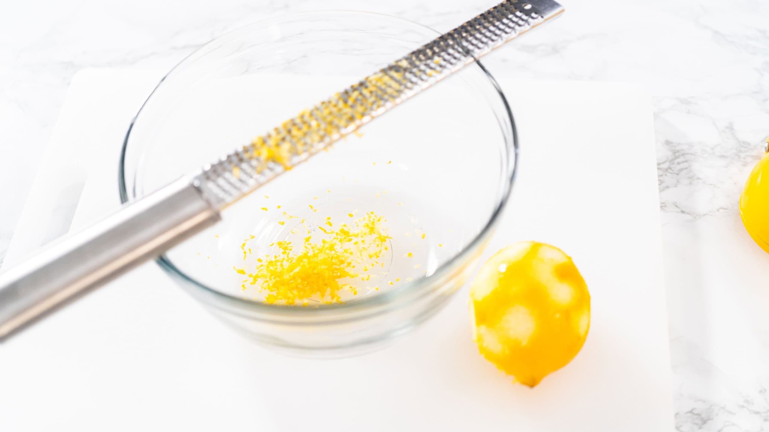 Zesting and juicing fresh lemon on a white cutting board.
