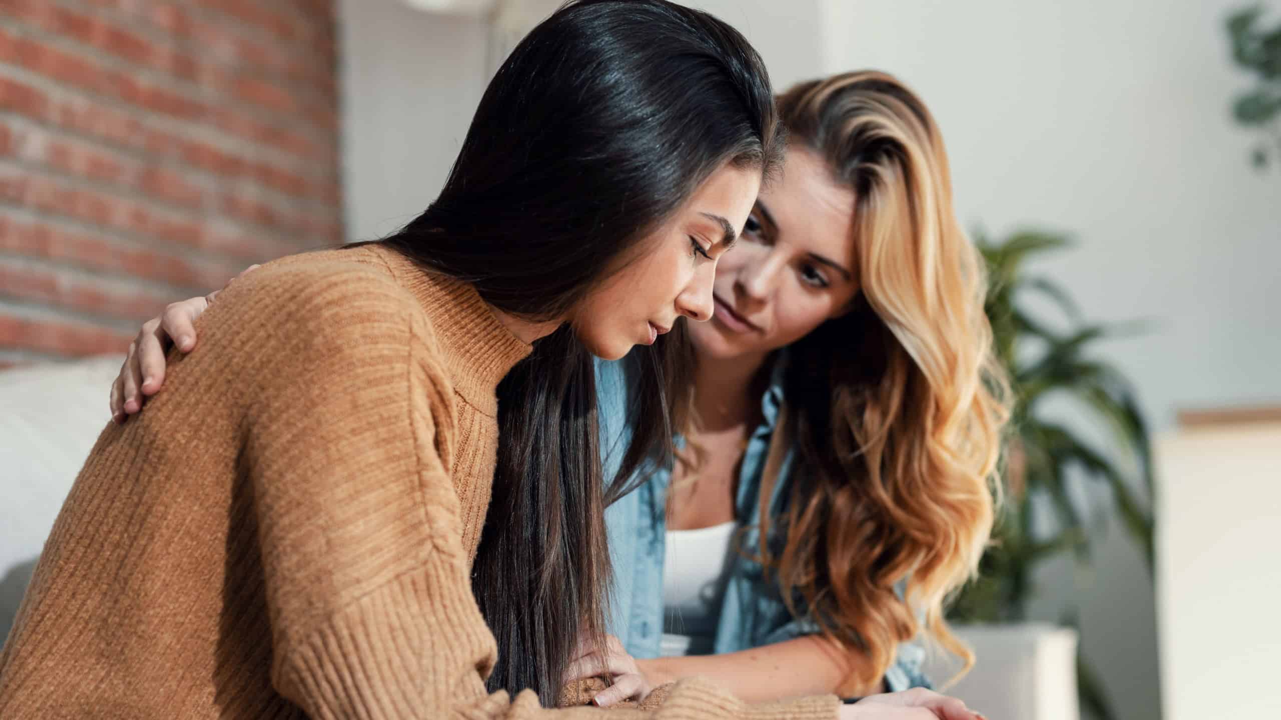 Shot of pretty young woman supporting and comforting her sad friend while sitting on the sofa at home.