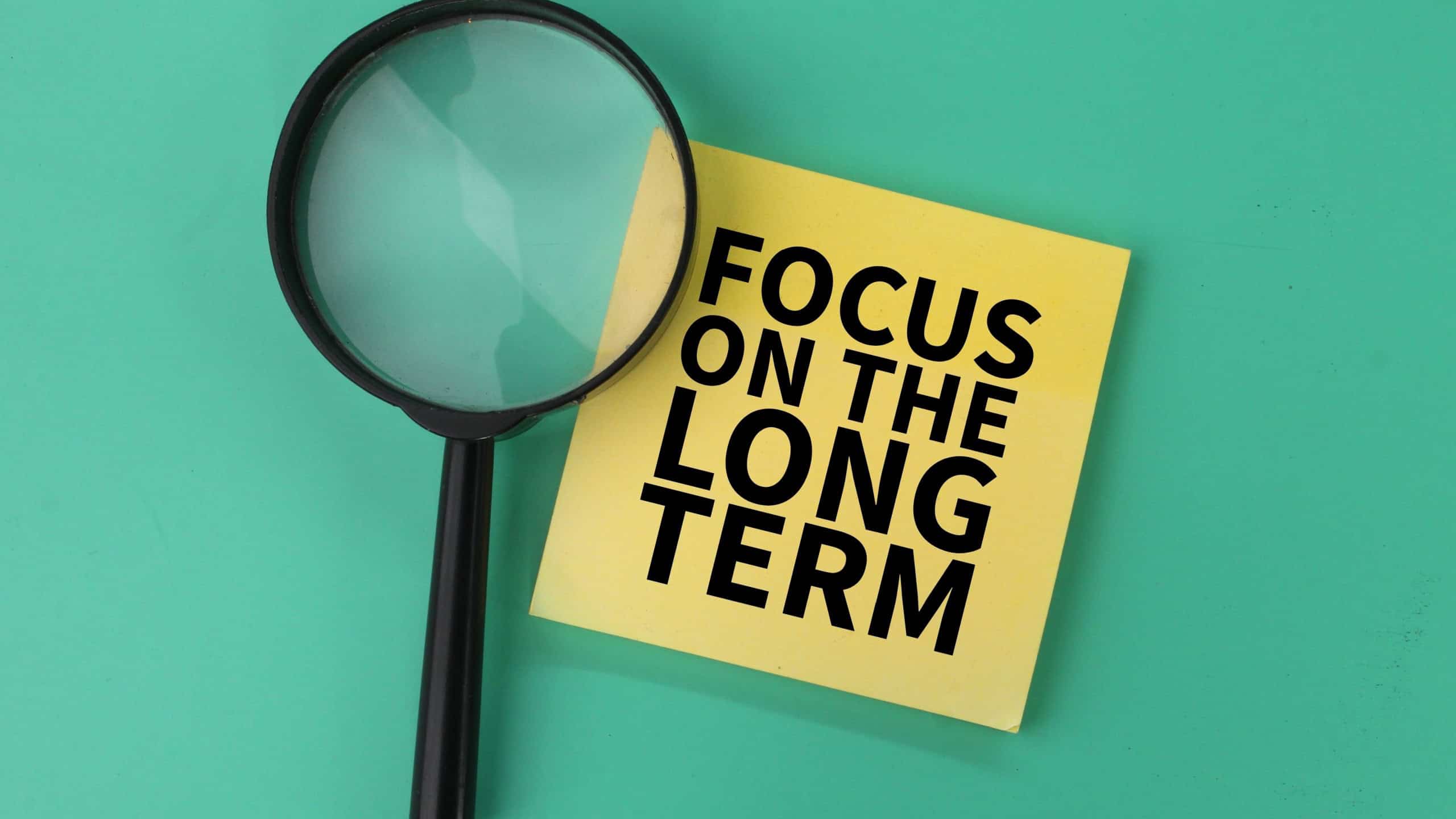 magnifying glass and colored paper with the words focus on the long term. LONG TERM INVESTMENT