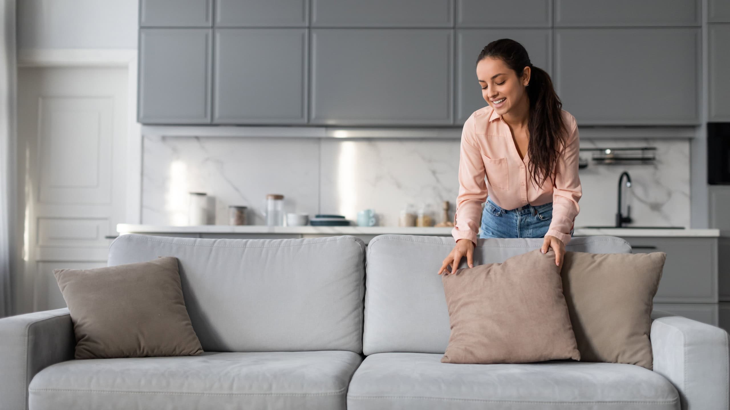 Content woman meticulously arranges decorative pillows on stylish couch, adding the finishing touches to her well-maintained contemporary living space