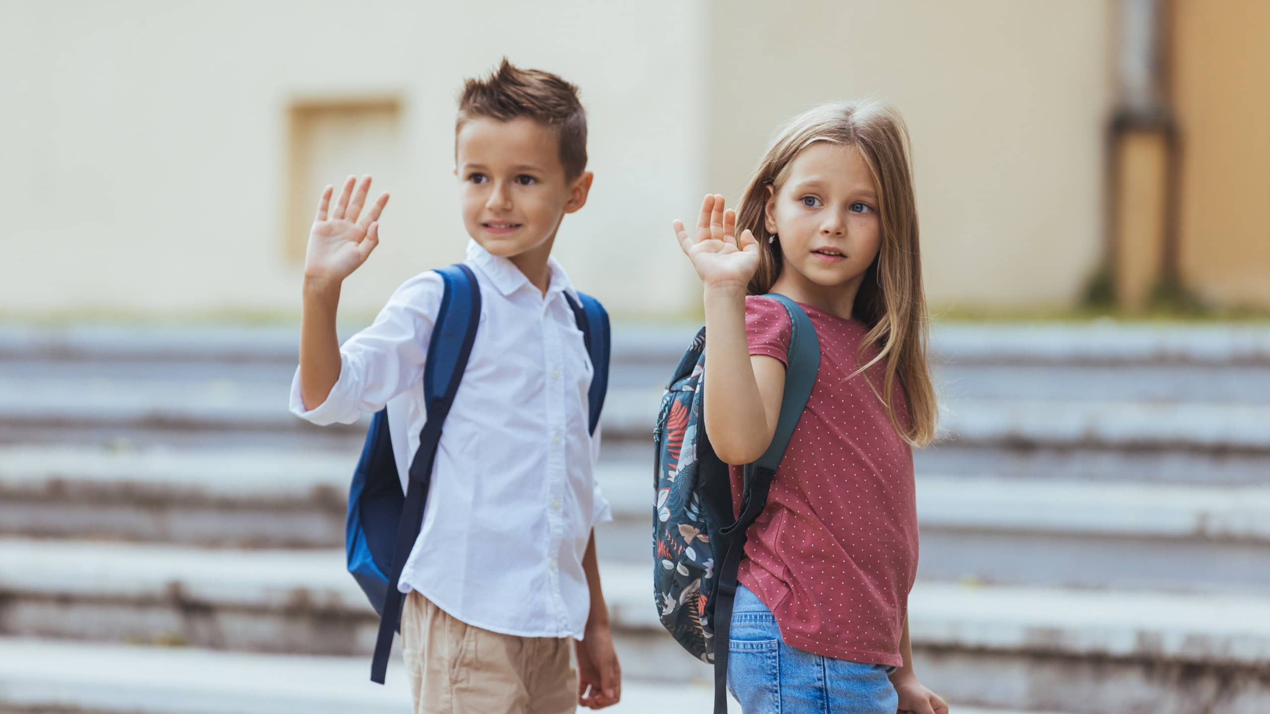 Schoolkids waving with hand to their mother, before entering the school building . Daughter and son is looking at woman standing outside the entrance of school. She is leaving her child to school.