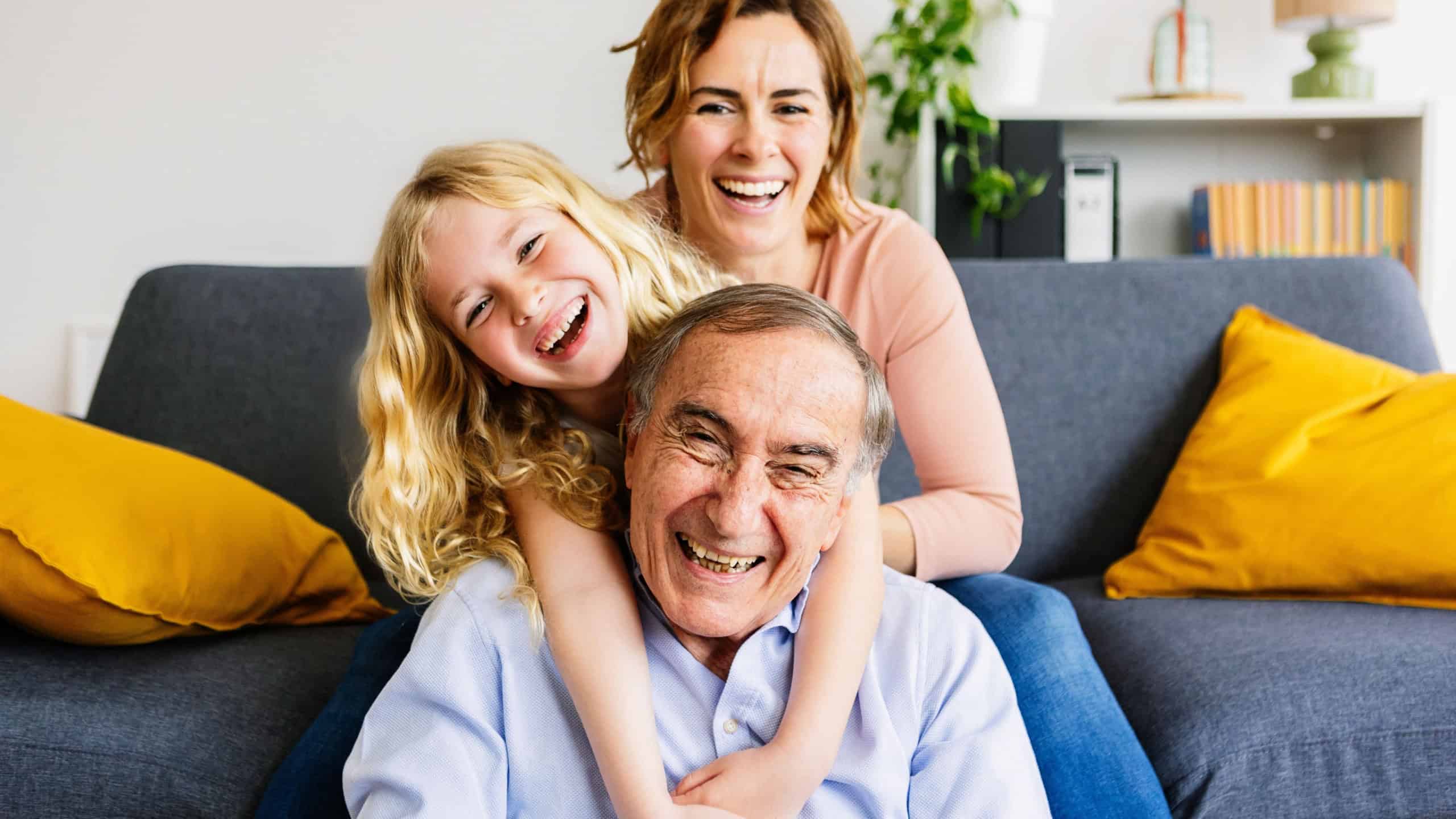 Cheerful portrait of little cute girl playing with her grandfather and mother at home. Happy family having fun.