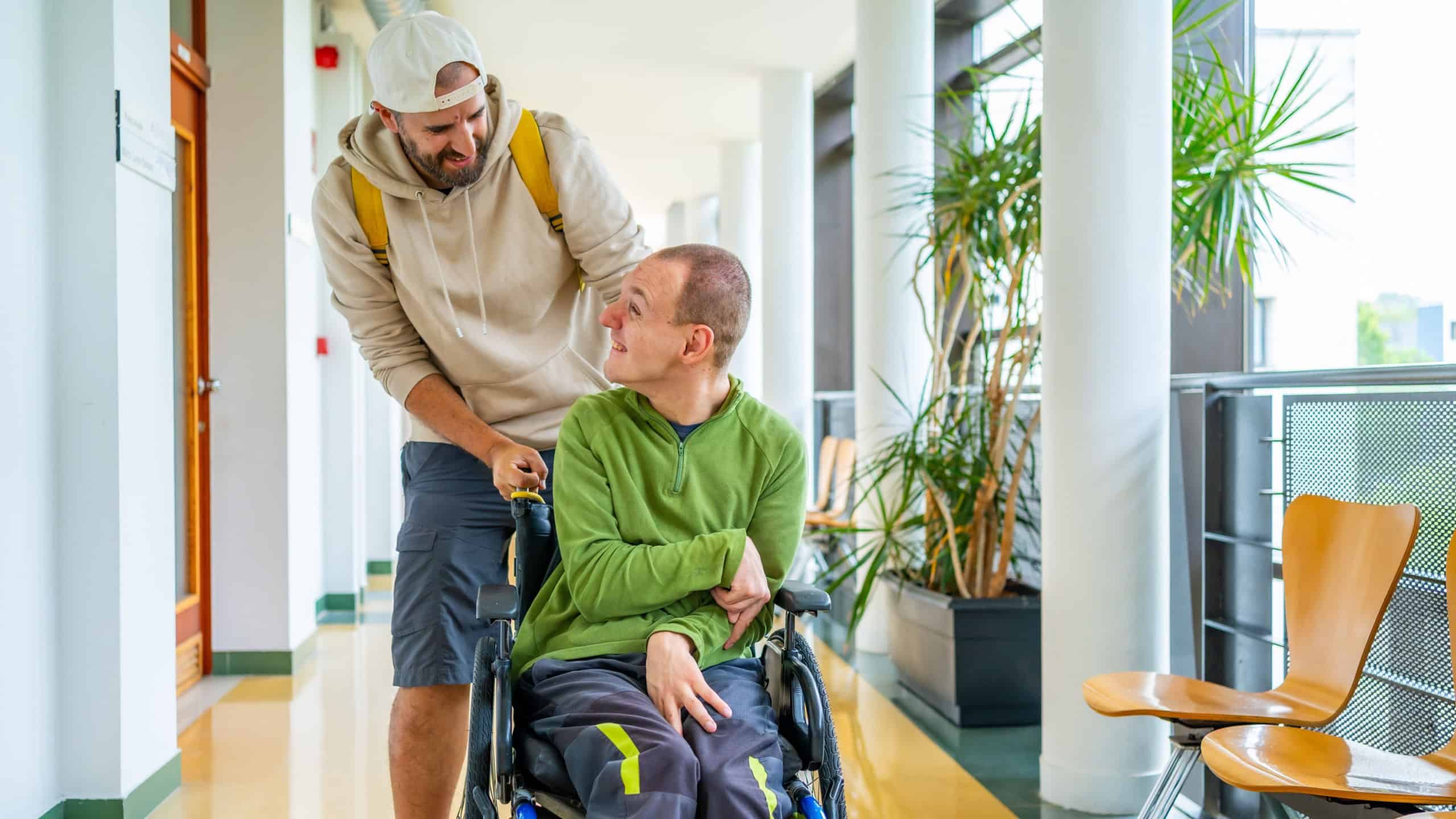 Caucasian young man pushing the wheelchair of a friend with disability around the university