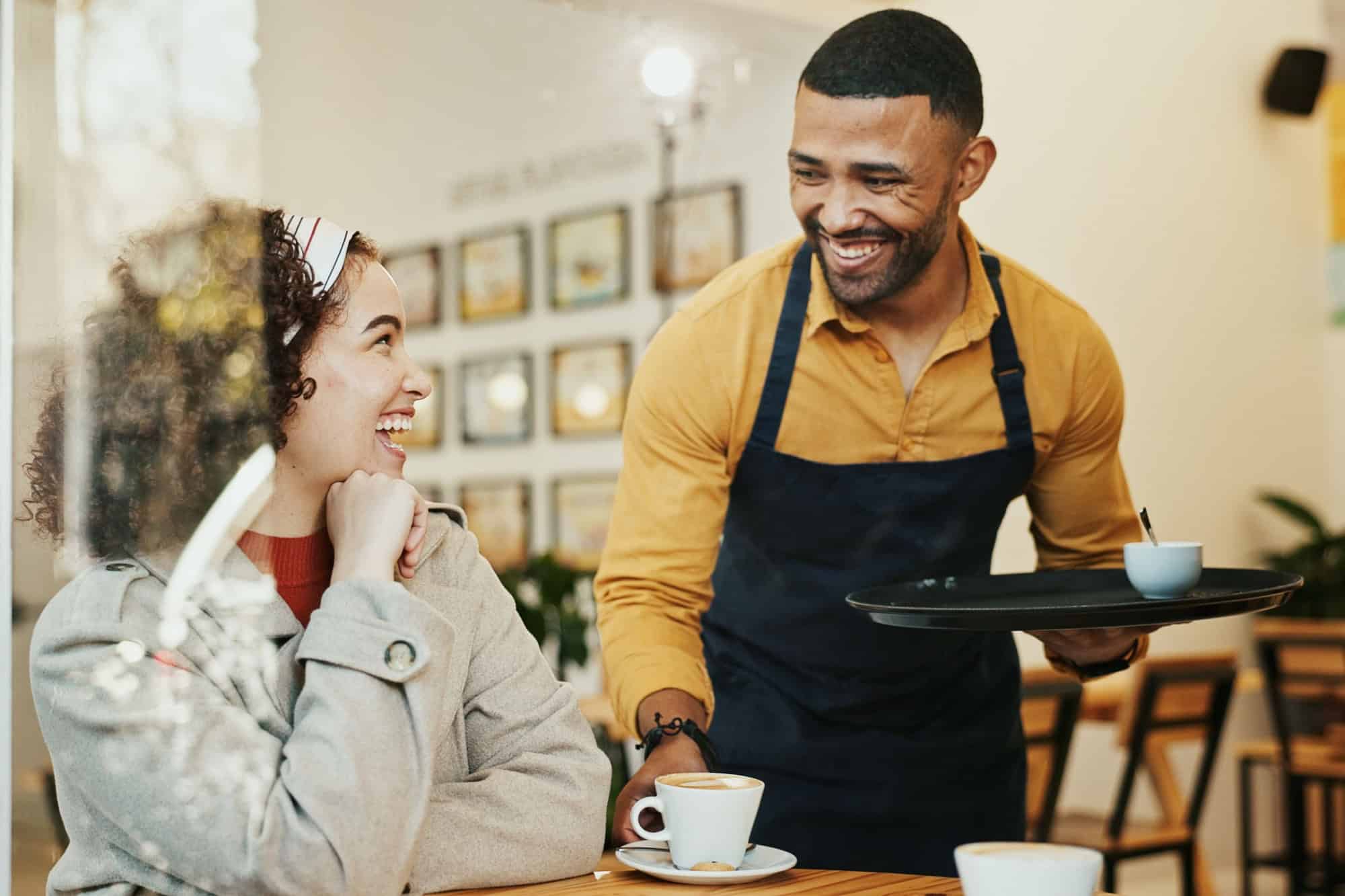 Cafe, women and waiter with coffee order, conversation and customer service at restaurant. Barista, staff and happy girl friends with smile and chat at diner with employee helping with hot drink