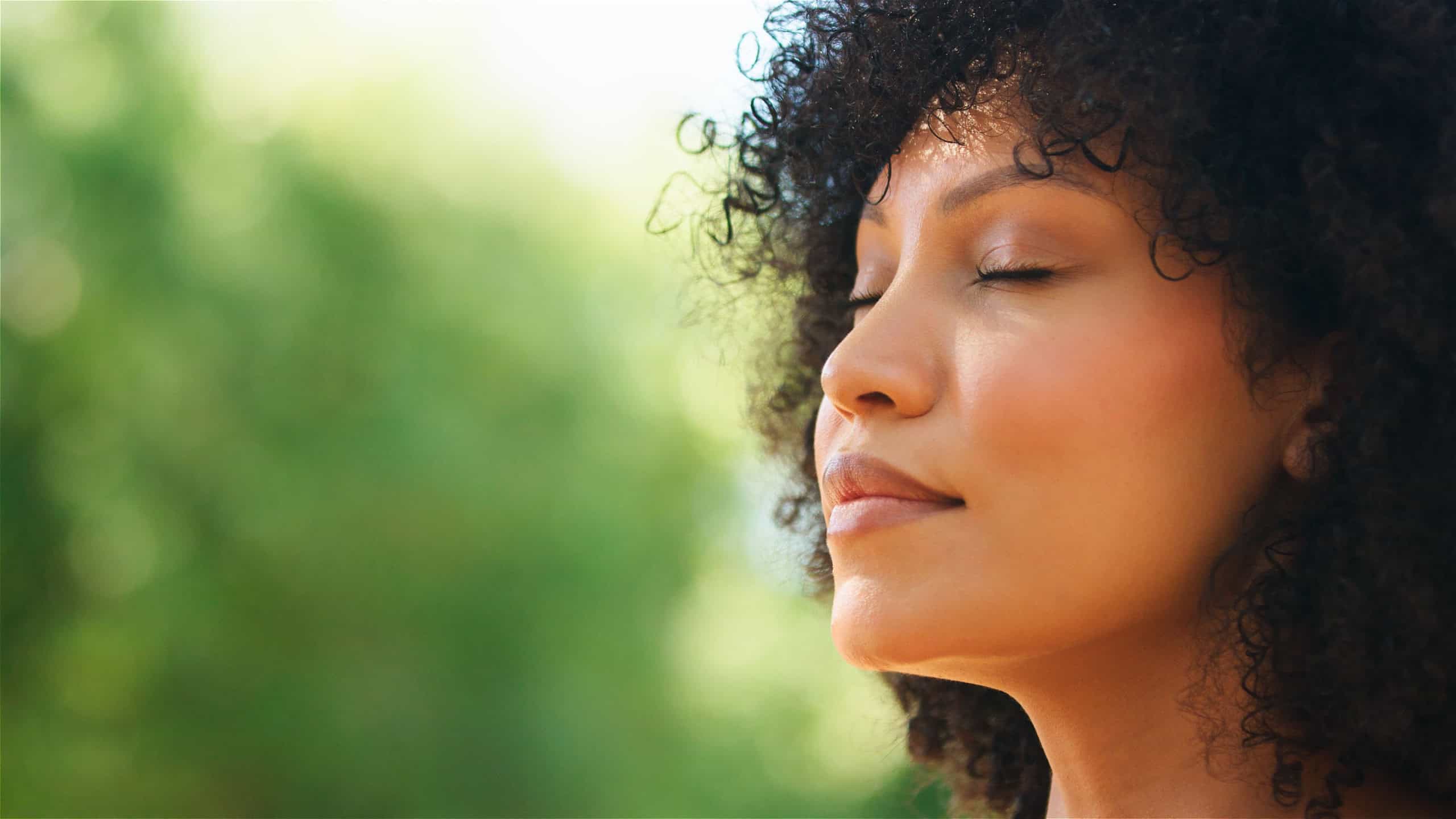 A woman enjoys peaceful meditation in a green outdoor area.