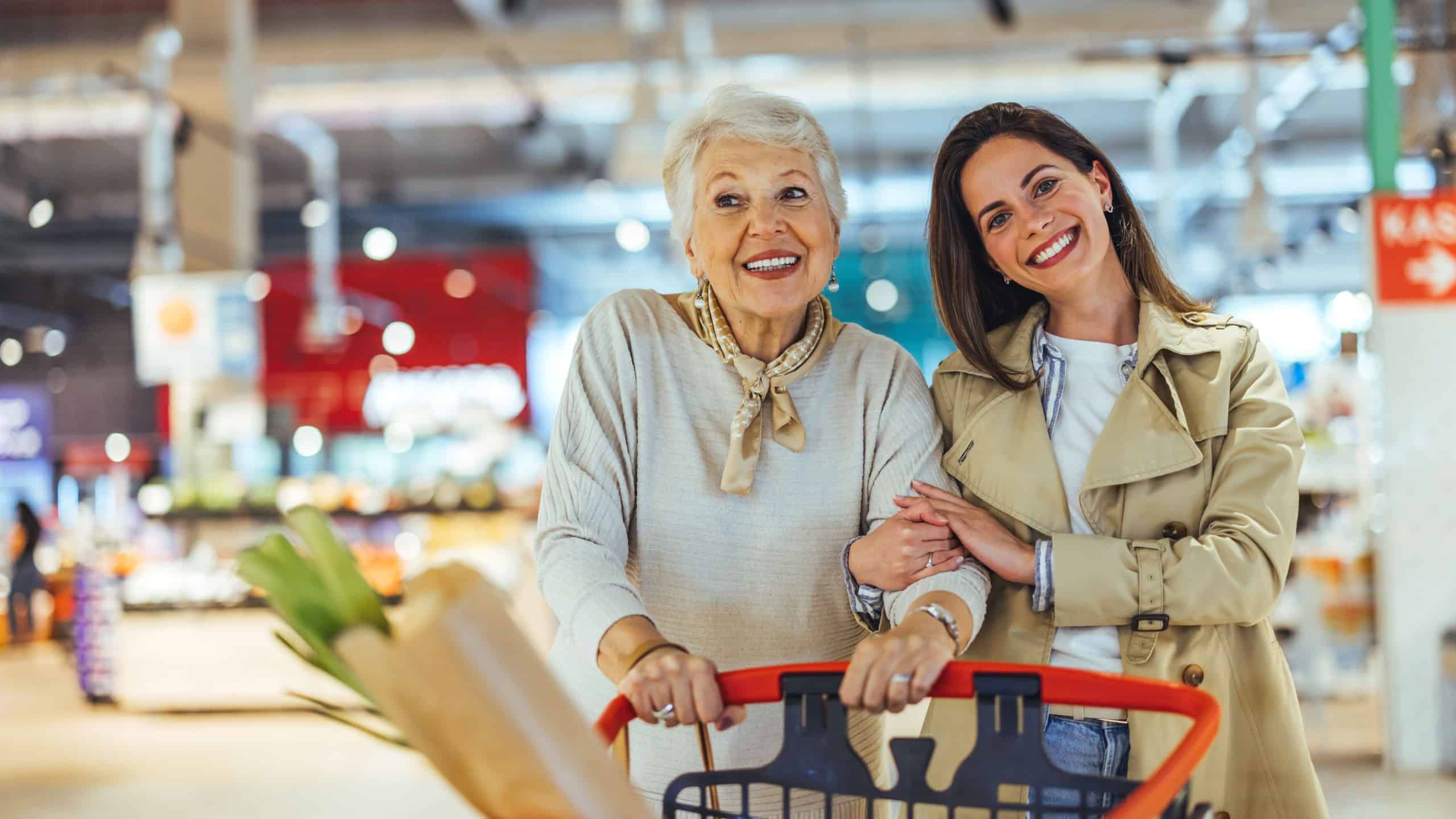 A joyful grandmother and granddaughter enjoy grocery shopping together in a supermarket. They are smiling and holding a shopping cart filled with fresh produce.