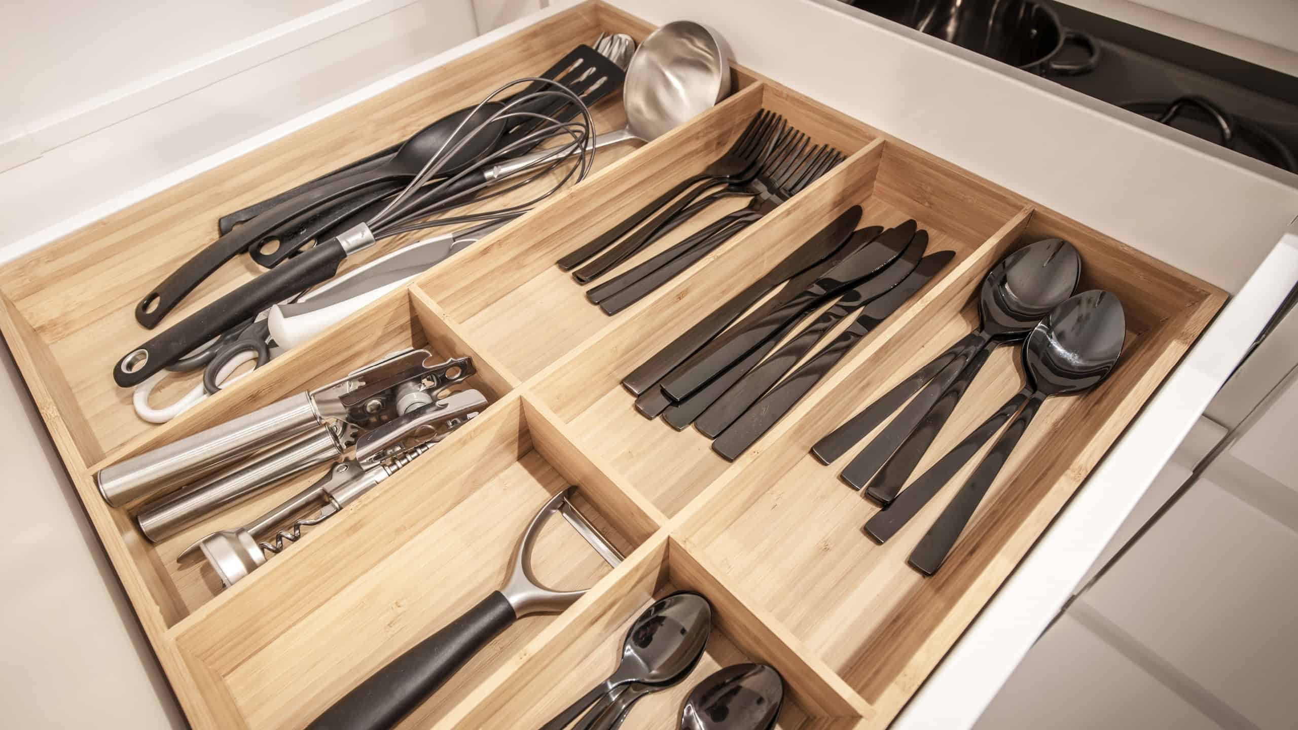 A well-arranged kitchen drawer showcases an assortment of utensils, cutlery, and tools, emphasizing cleanliness and modern organization within a sleek wooden divider.
