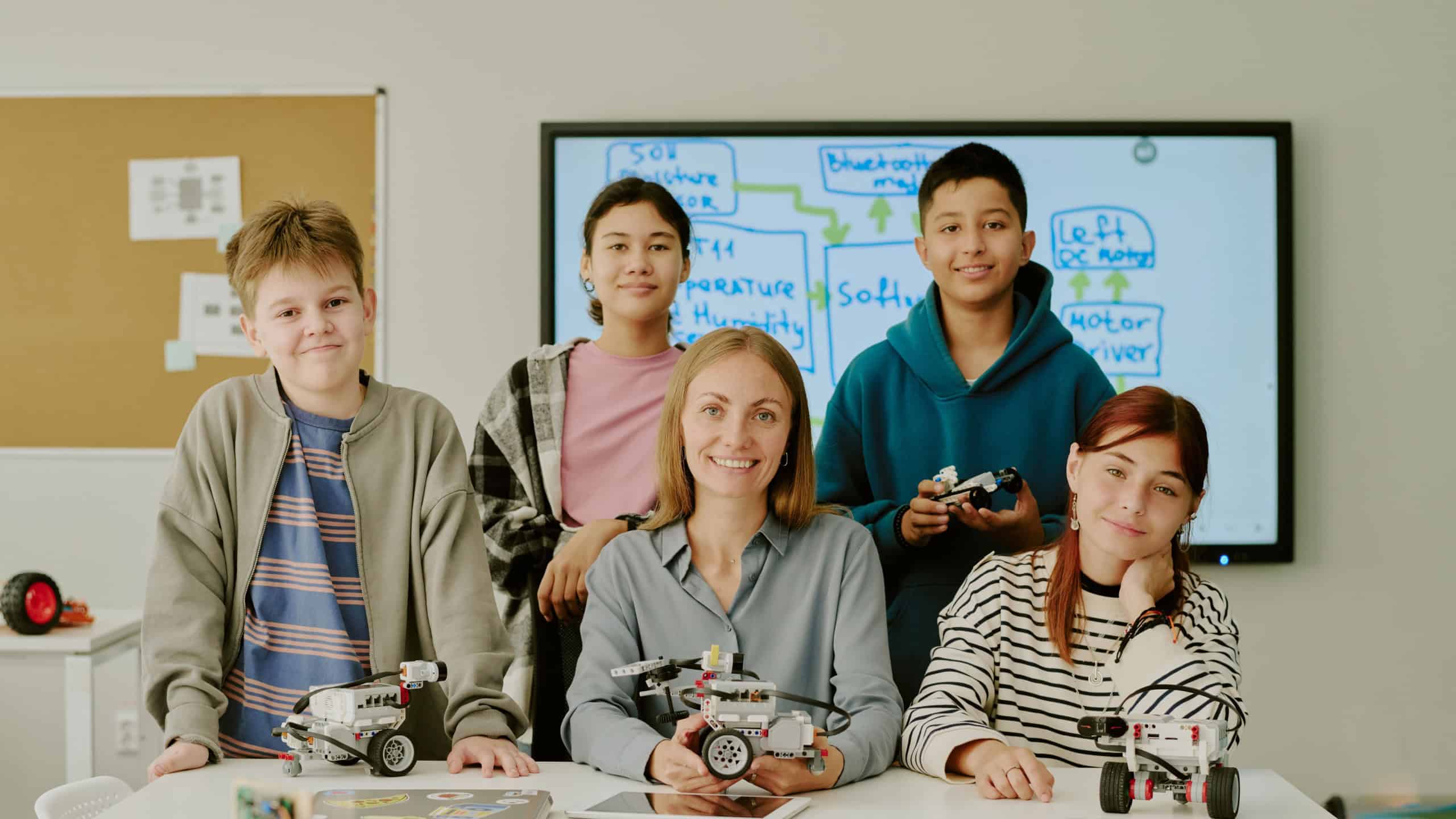 Portrait of multiracial students with their favorite robotics teacher with prototype in hands posing for photo in light classroom