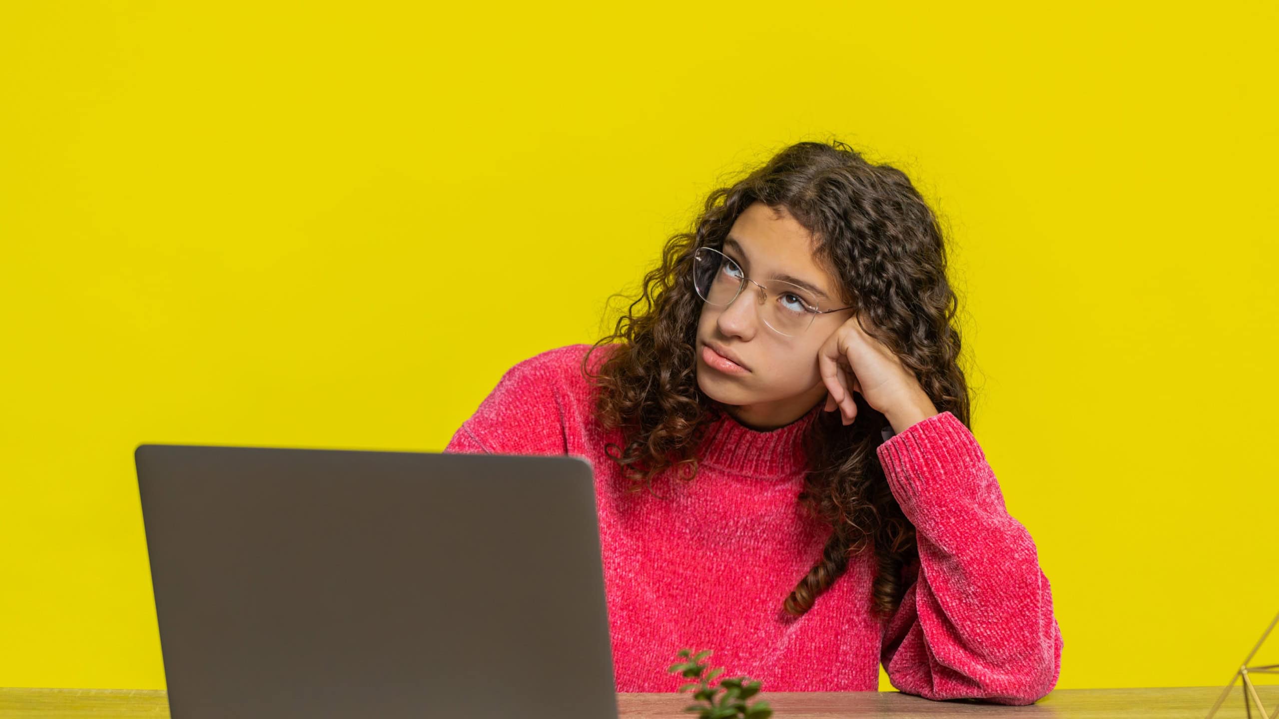Tired bored stressed Caucasian young teenager girl using laptop feeling annoyed during study or work. Exhausted teen child kid remote distance education sitting on table isolated on yellow background