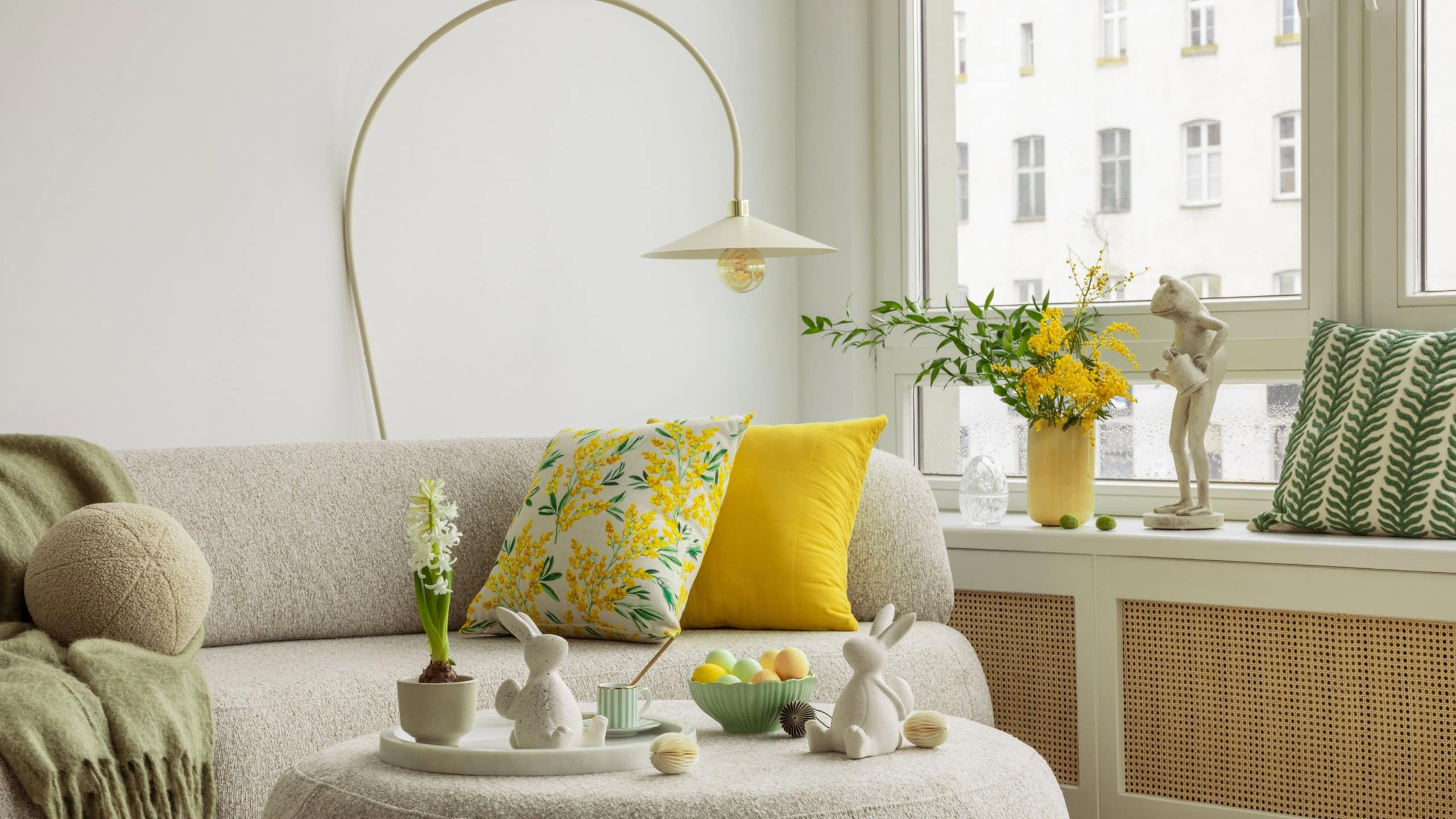 Interior design of spring living room with design sofa, furniture, vase with tulips, easter decorations, pillows and personal accessories. Home decor. Template. Easter holidays.