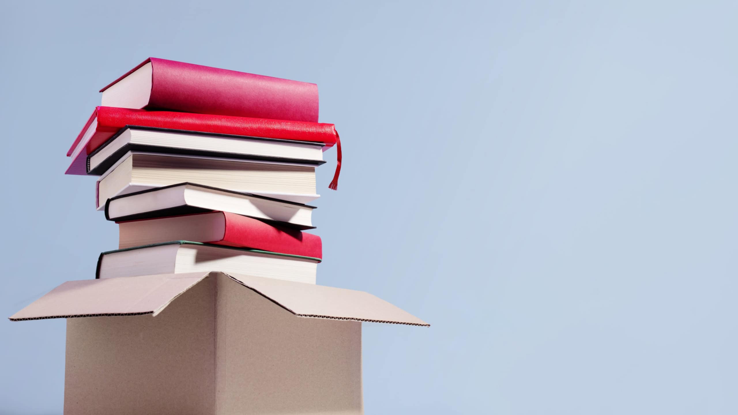 Used second-hand books in a box ready for donation against a blue background, minimal style still life. Concept of books donations, educational charity, copy space