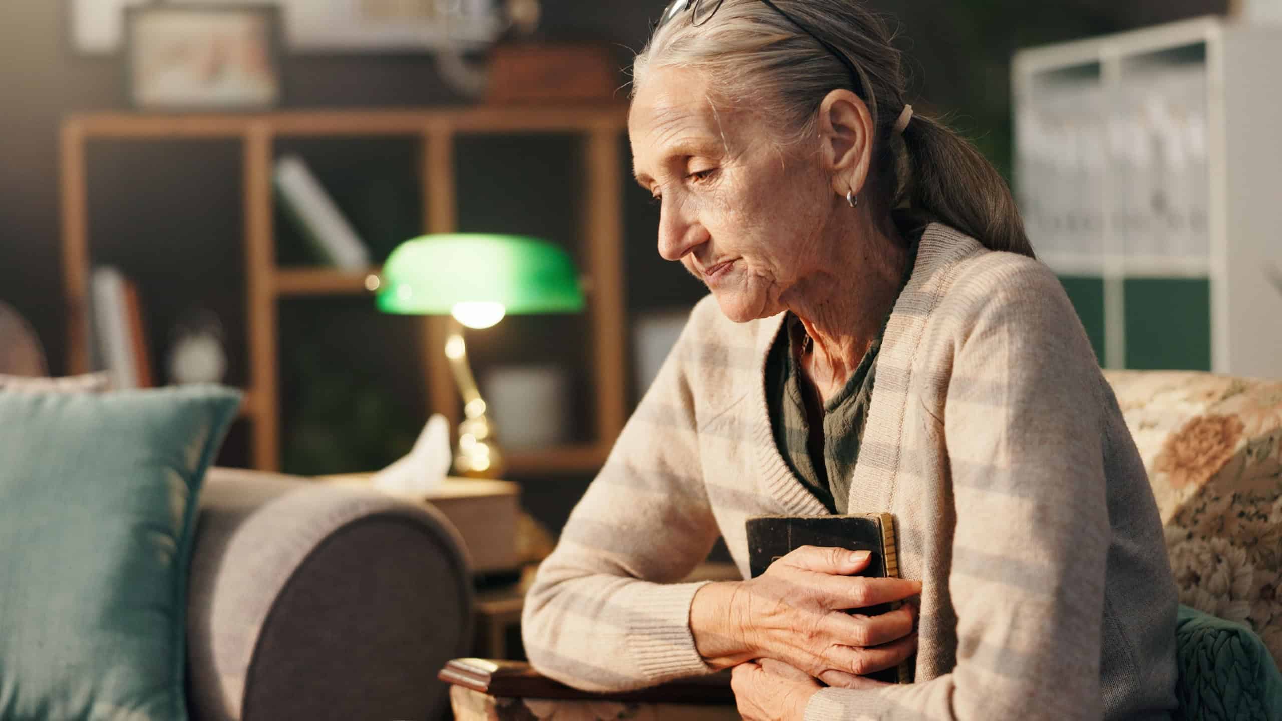 Sad, old woman and thinking with picture frame in home for mourning, grief and lonely in retirement. Senior widow, person with depression and hug photo on sofa for nostalgia, memory or broken heart