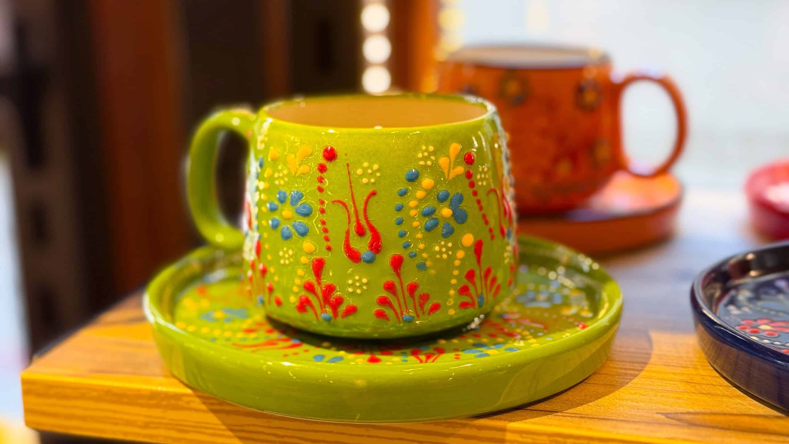 Bright green ceramic cup with floral ornament placed on matching saucer in a shop. Handcrafted artisan design, decorative tradition, and cultural craft symbolism