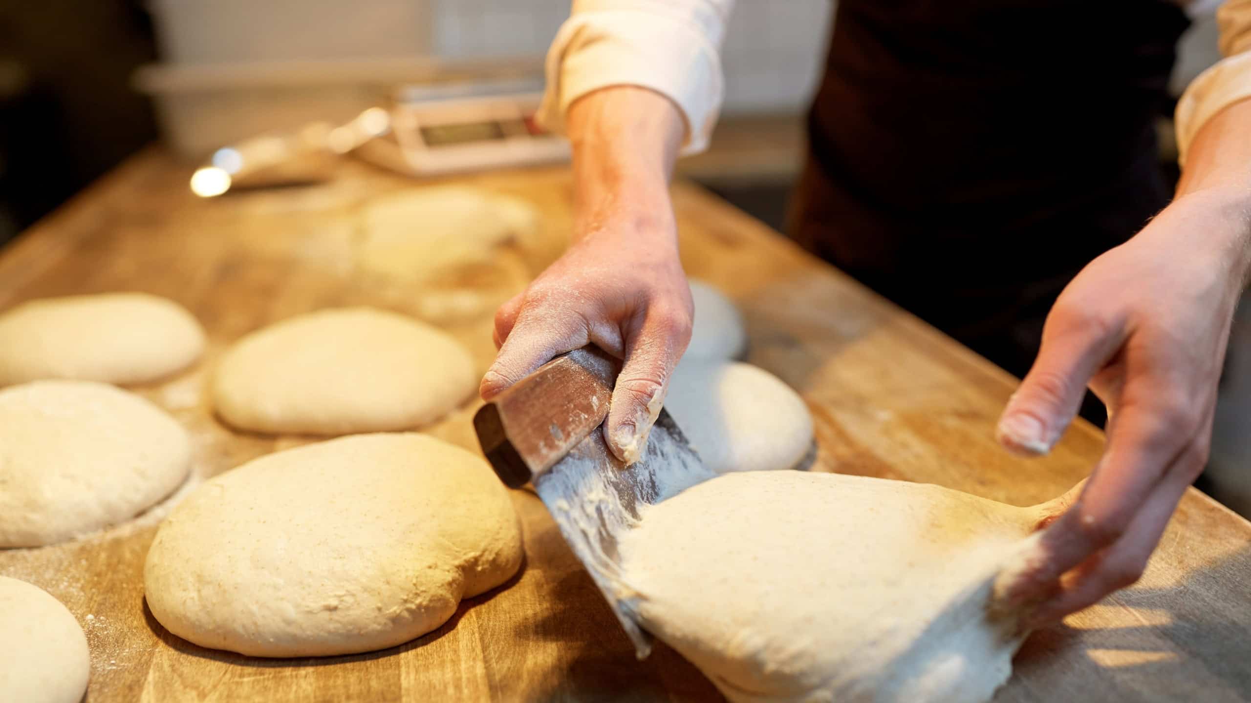 food cooking, baking and people concept - chef or baker portioning dough with bench cutter at bakery
