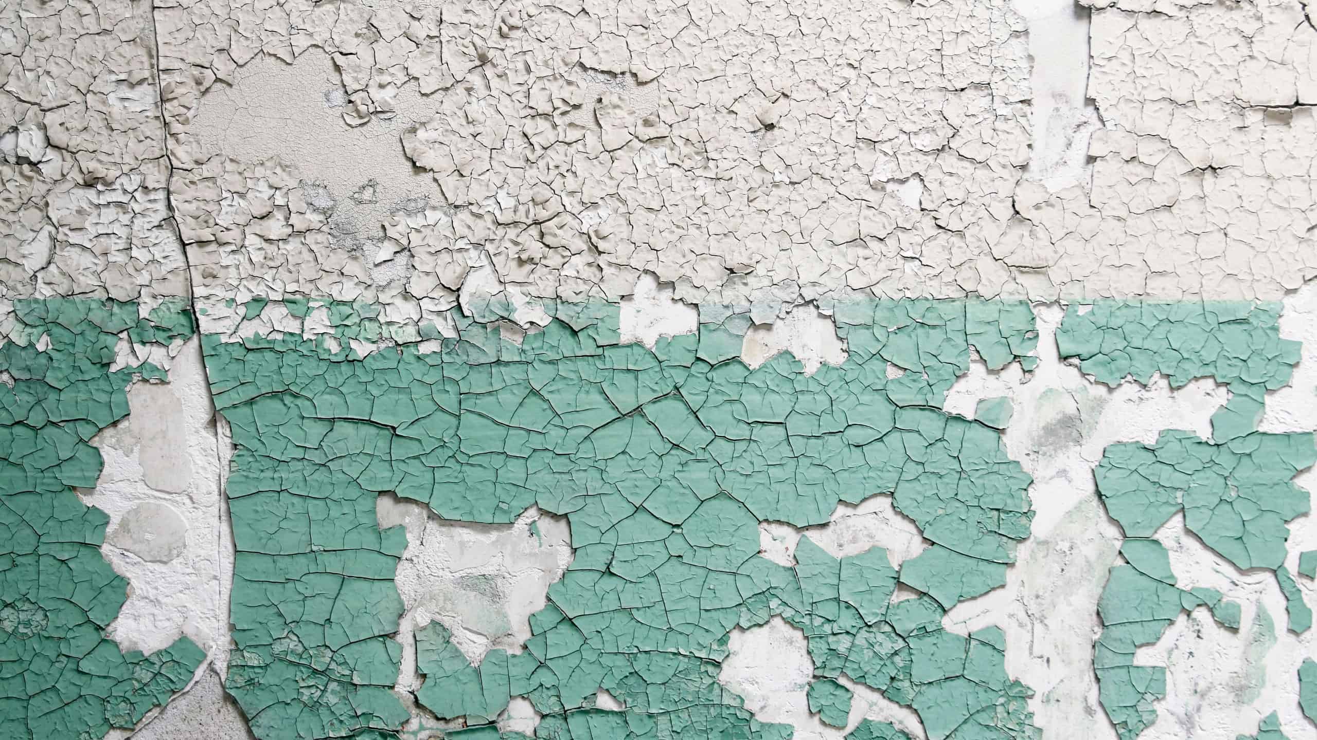 Cracked and distressed painted surface on the side of a building or wall. Concrete or cement texture with aged paint peeling off.