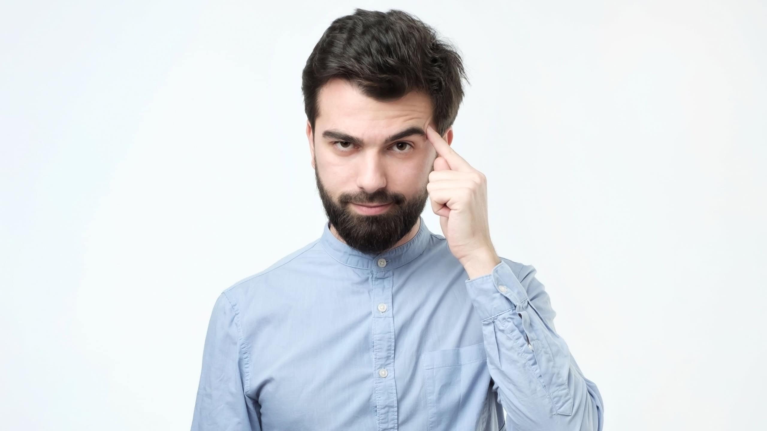 Let me think. Serious hispanic man with beard, keeps index finger on temple, recollect something in mind, remembers information