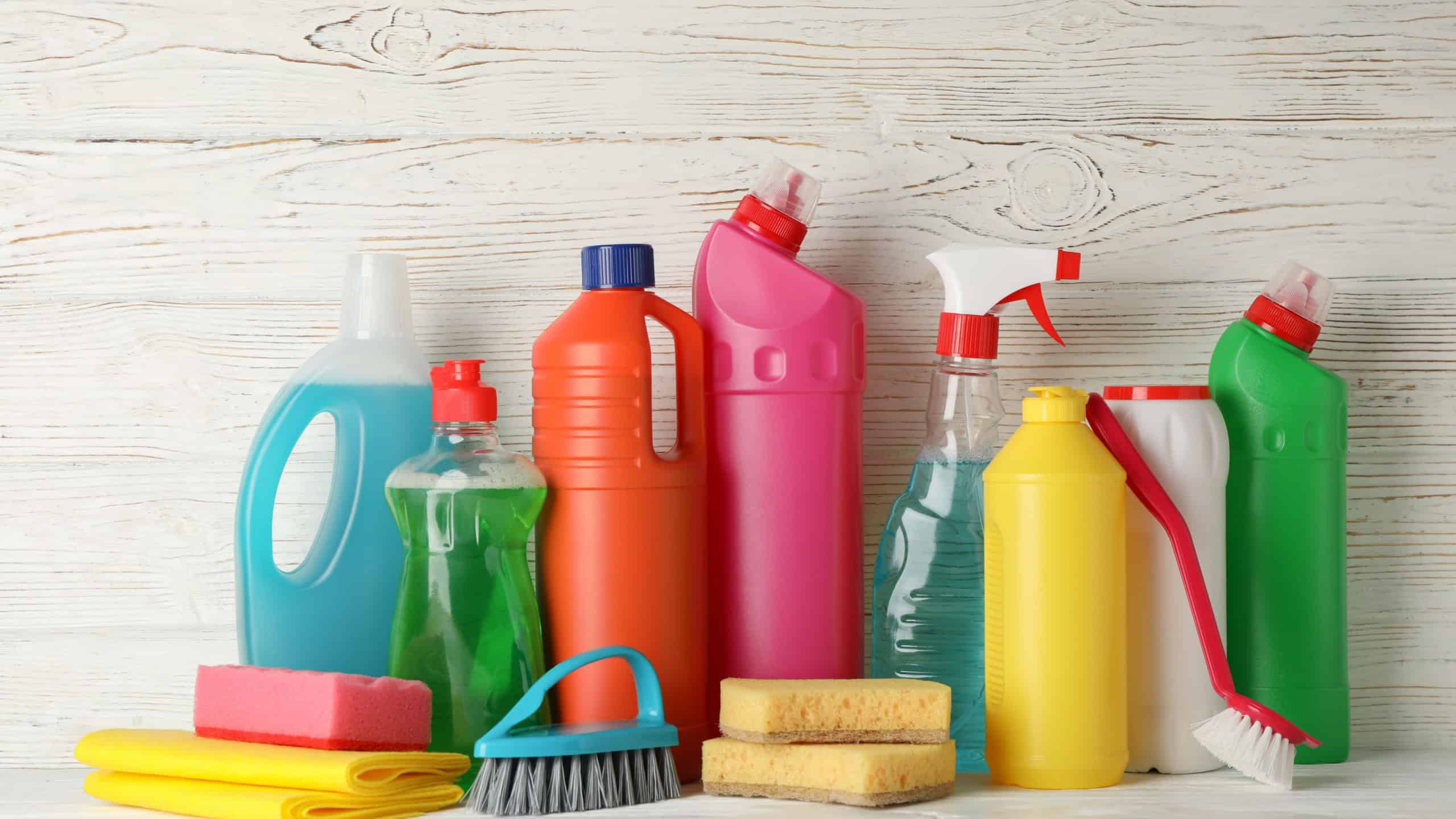 Bottles with detergent and cleaning supplies on wooden background, space for text