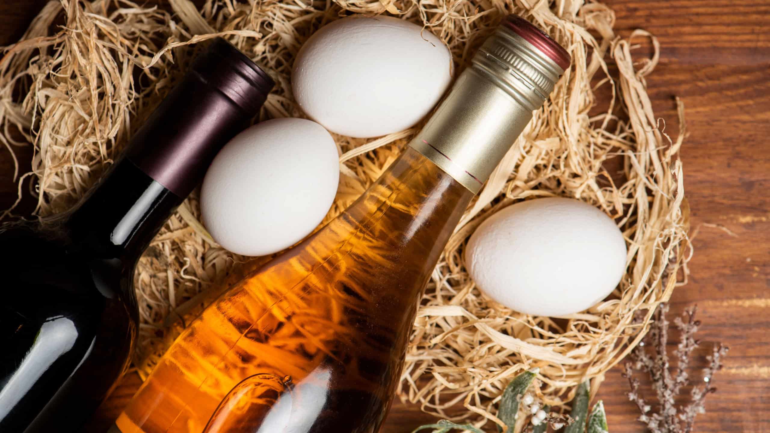 Wine bottles and chicken eggs in hay on the wooden background.
