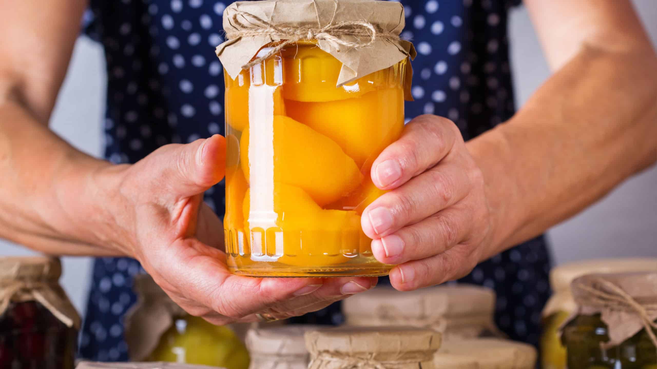 Senior mature woman holding in hands jar with homemade preserved and fermented food. Variety of pickled and marinated vegetables, fruit compote. Housekeeping, home economics, harvest preservation