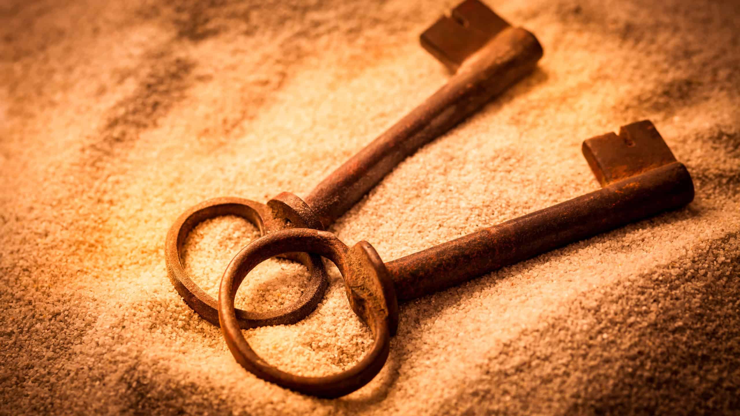Two old rusty keys in sand in warm tones
