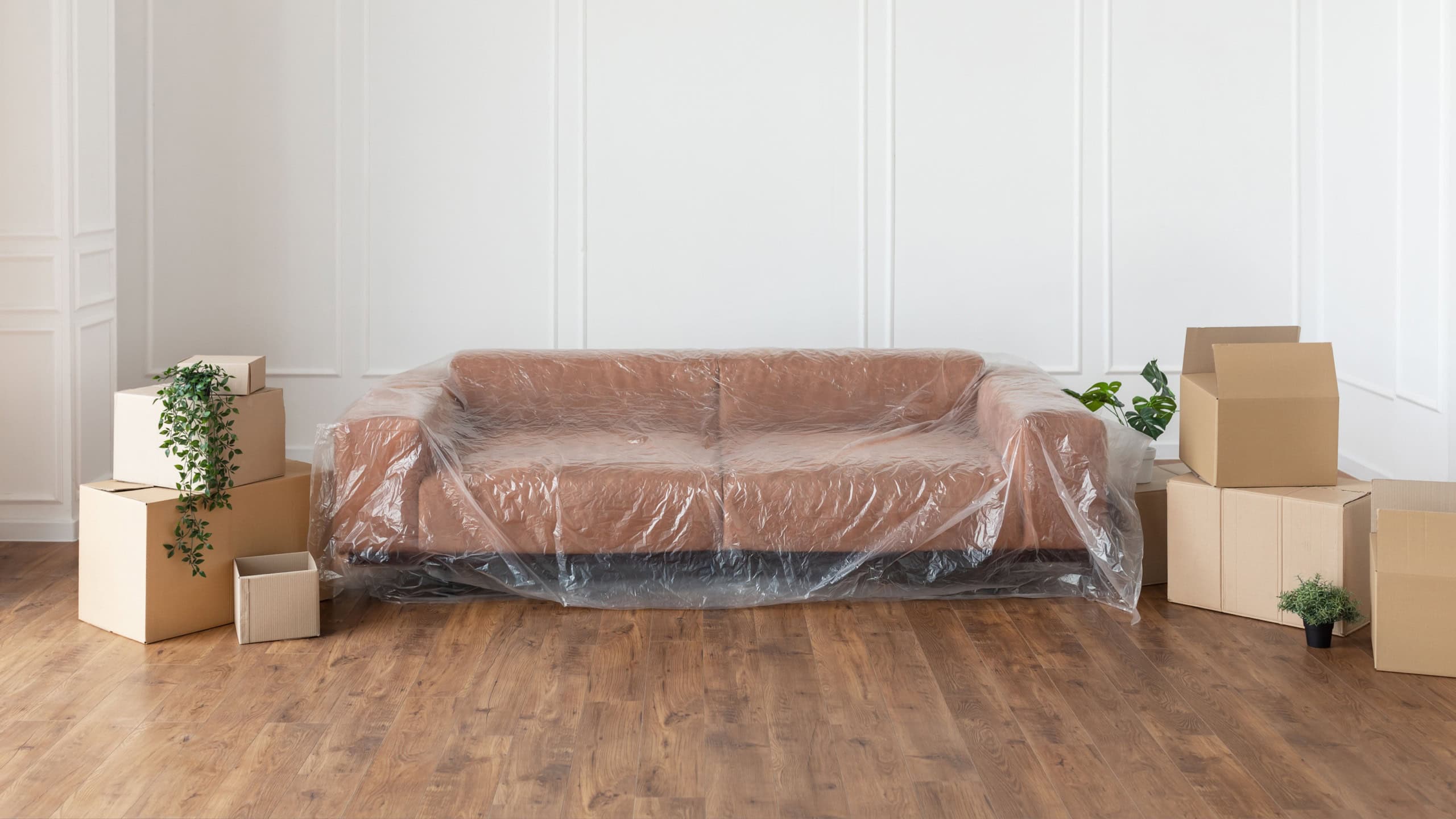 Relocation And Repair Concept. Modern stylish sofa covered with plastic sheet for home decorating. Apartment redecoration and home construction while renovating and improving flat, free copy space