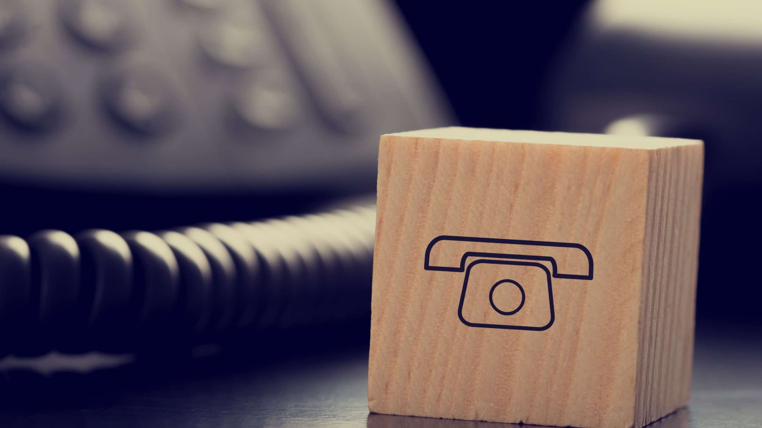 Retro Image of Wooden Block with Graphic of Old Fashioned Telephone in front of Other Black Telephone.