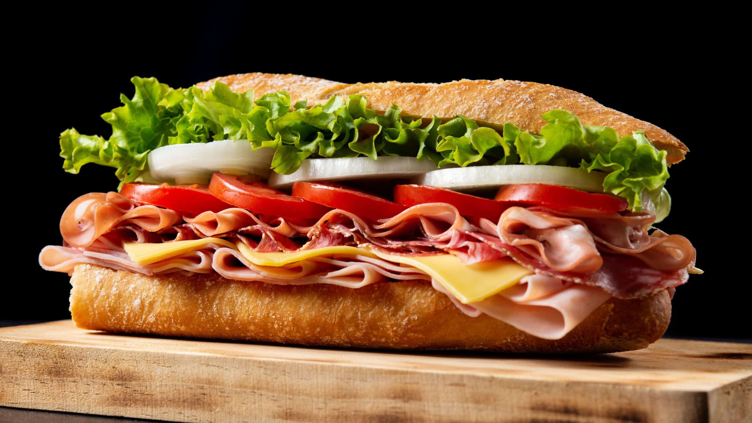 Submarine sandwich with ham, cheese, lettuce, tomatoes,onion, mortadella and sausage on wooden table