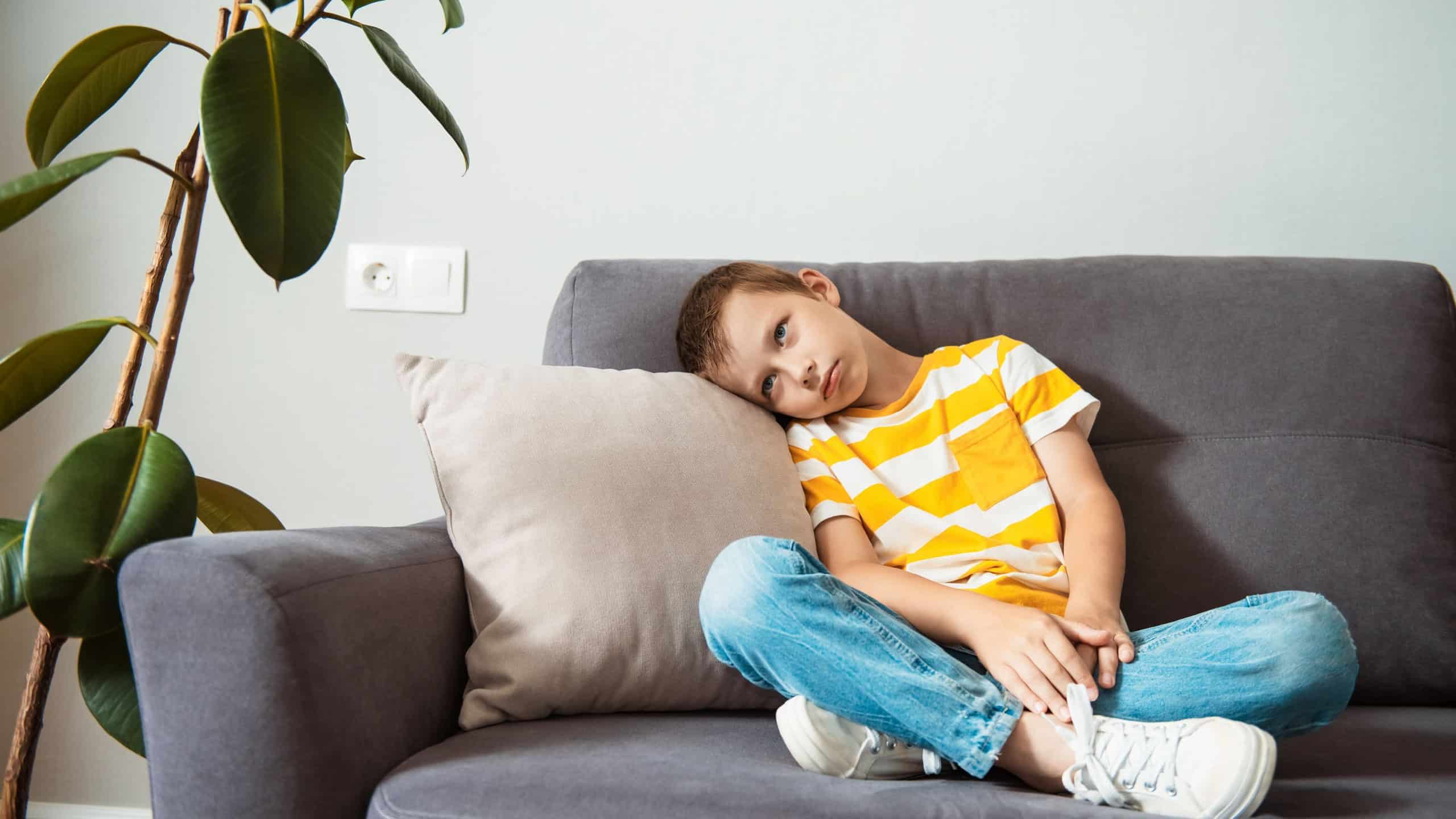 Little boy sitting on a couch and upset with a bored face