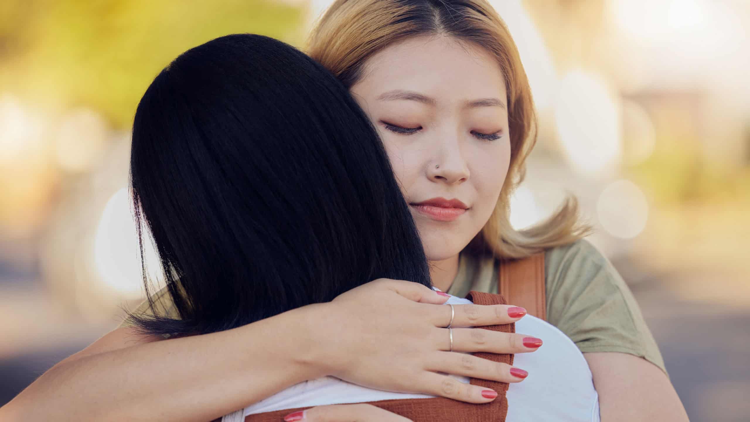 Woman, friends and love hug in city outdoors together for sorry, support and lesbian couple forgive in street. Asian people, friendship and emotional hugging for grief or sadness in urban city street